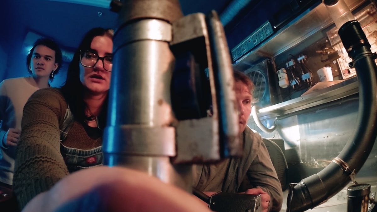 A fish eye view of three people solving a puzzle.  One is holding a metal rod close to the camera.