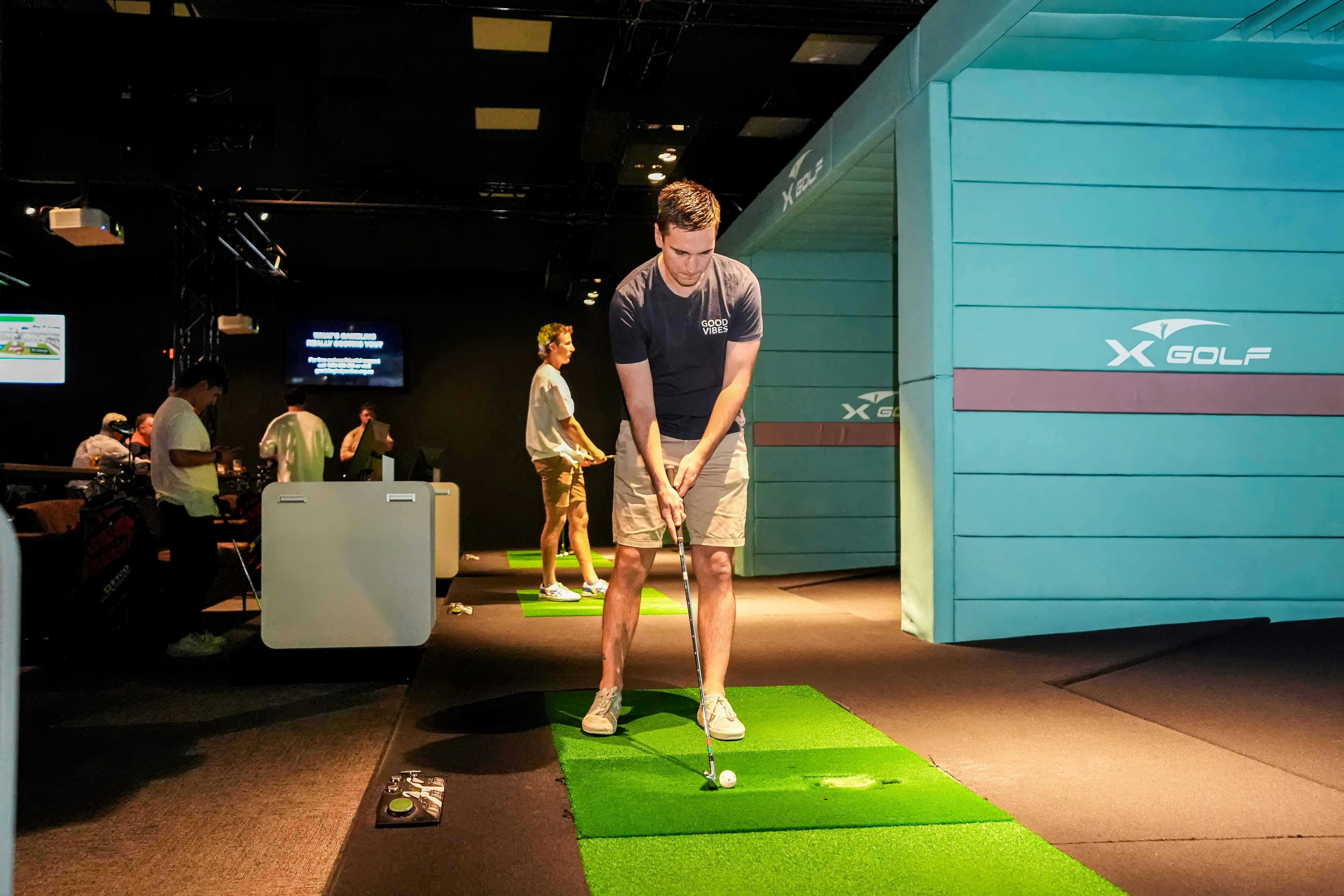 A man in shorts is hitting a golf ball at an indoor golf business