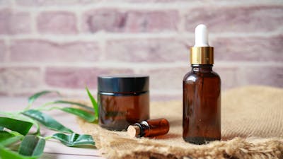 Three glass oil bottles on jute fabric and a sprig of palm leaf to the left