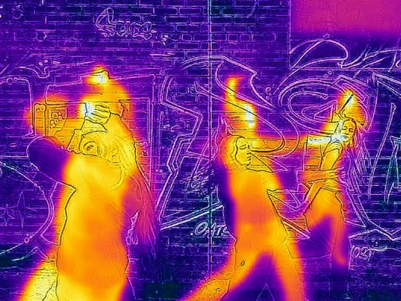 Three performers dance in front of a graffiti-covered brick wall, rendered in a vivid infrared-style