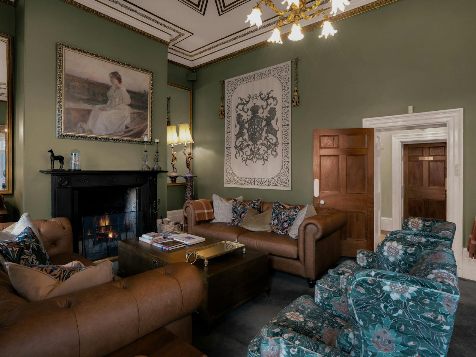 Green painted room filled with plush furniture in front of a roaring  open fire place