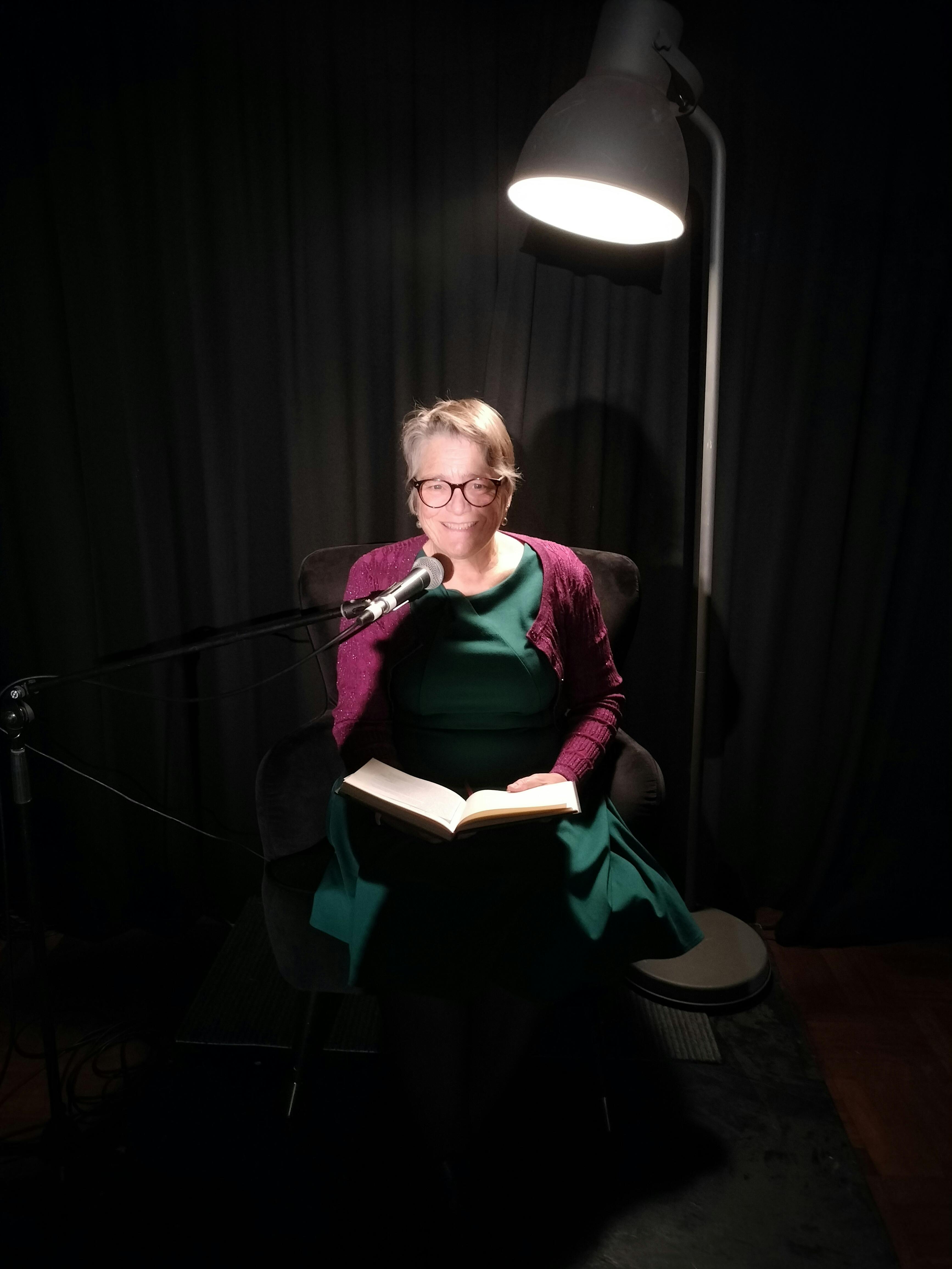 Woman in green dress and purple cardigan sitting in armchair with book lying on lap