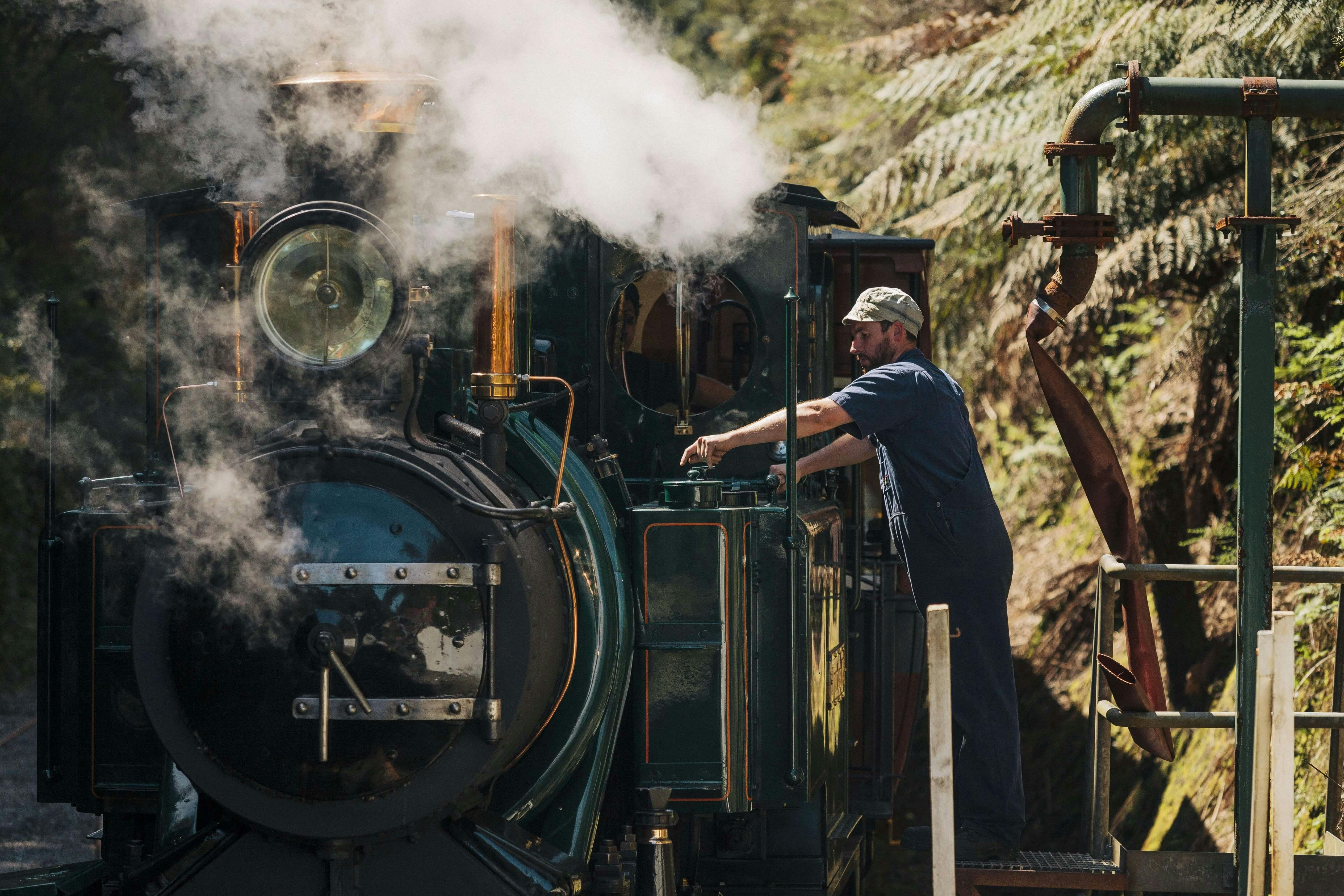 A driver in blue uniform and cap refills the green locomotive in steam