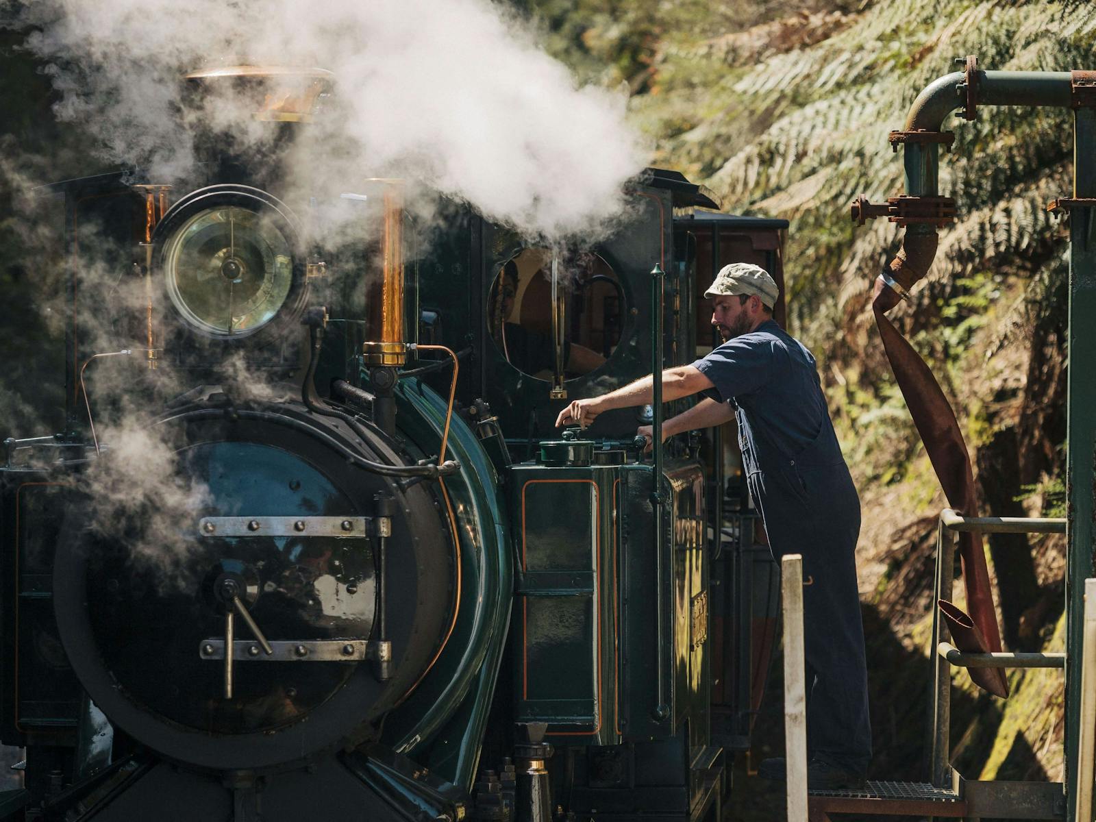 A driver in blue uniform and cap refills the green locomotive in steam
