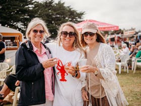 Three ladies with drinks in hand at the festival - the middle with a crayfish on her T-shirt