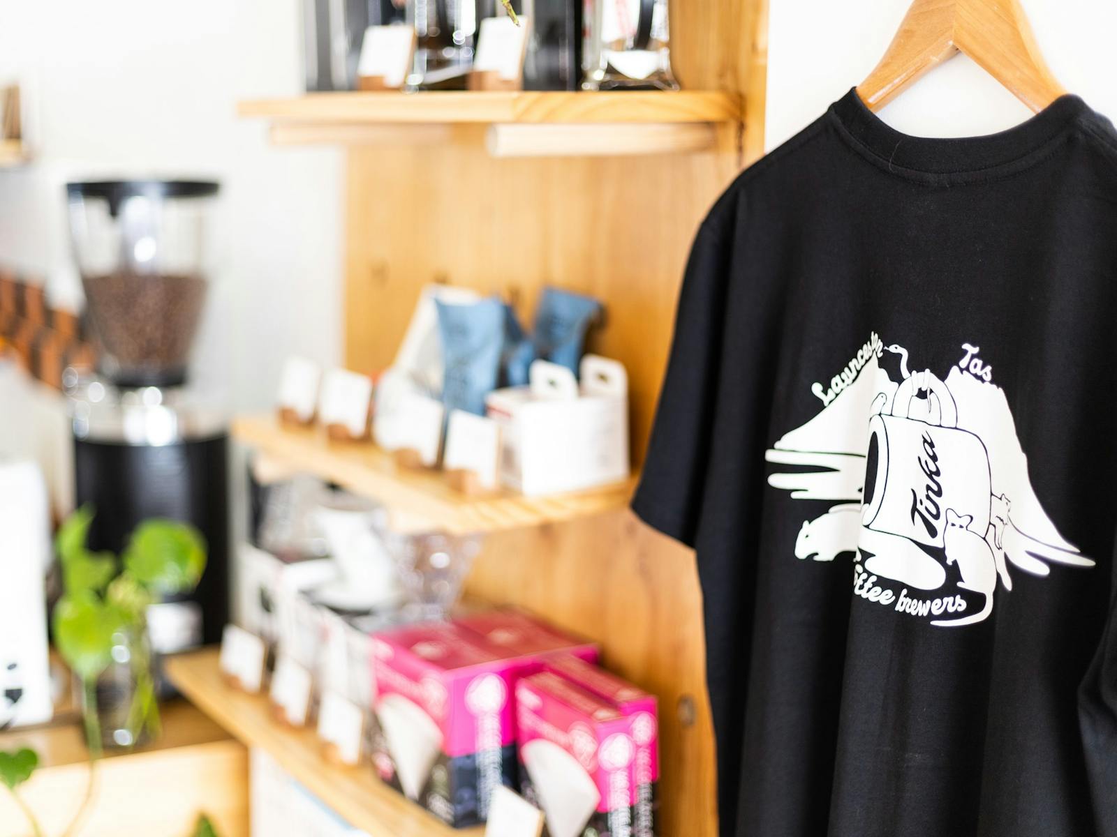 A black Tinka tee in the front of the frame and shelves full of coffee making equiptment in the back