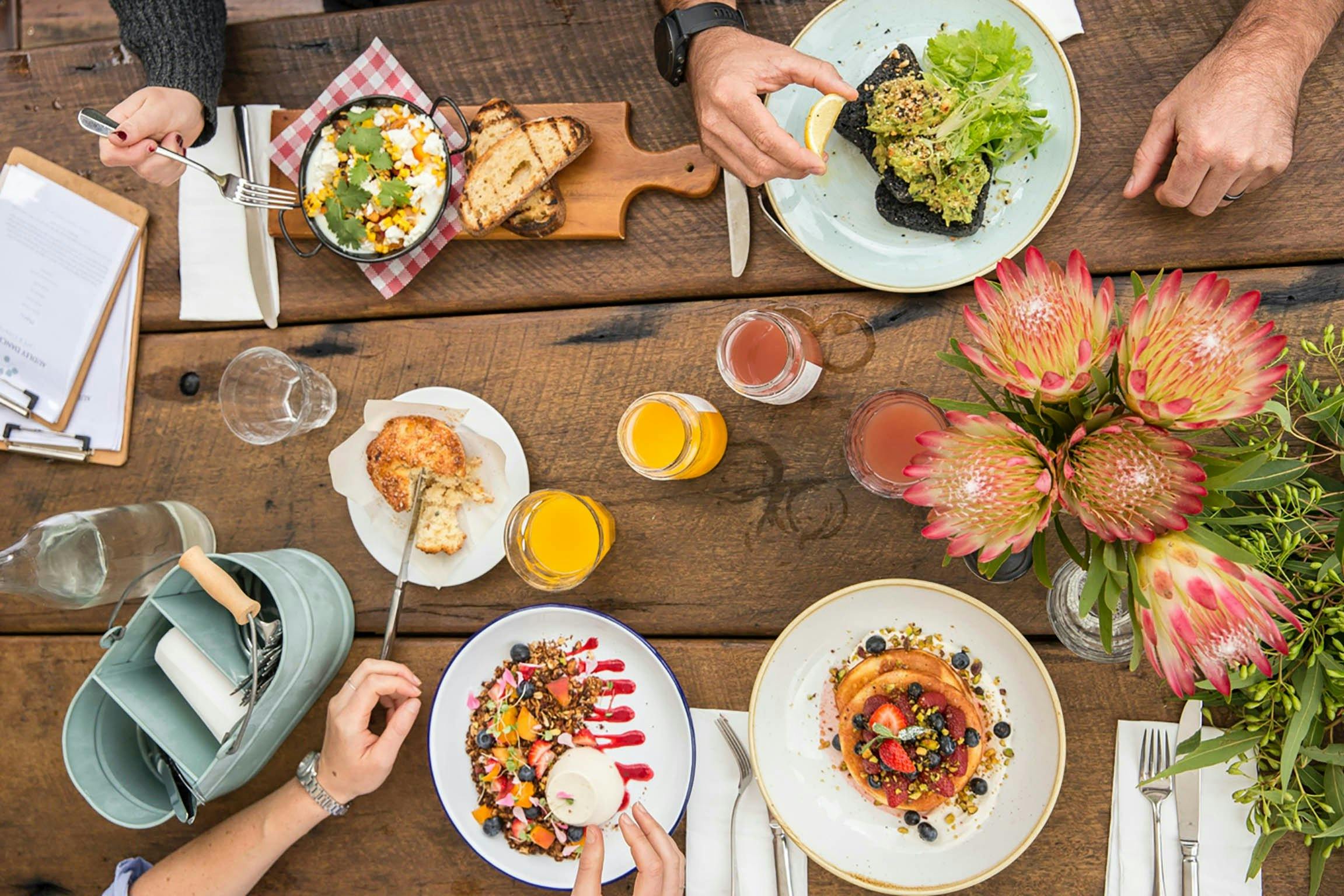 birds-eye shot of pancakes avo toast baked eggs  on timber table