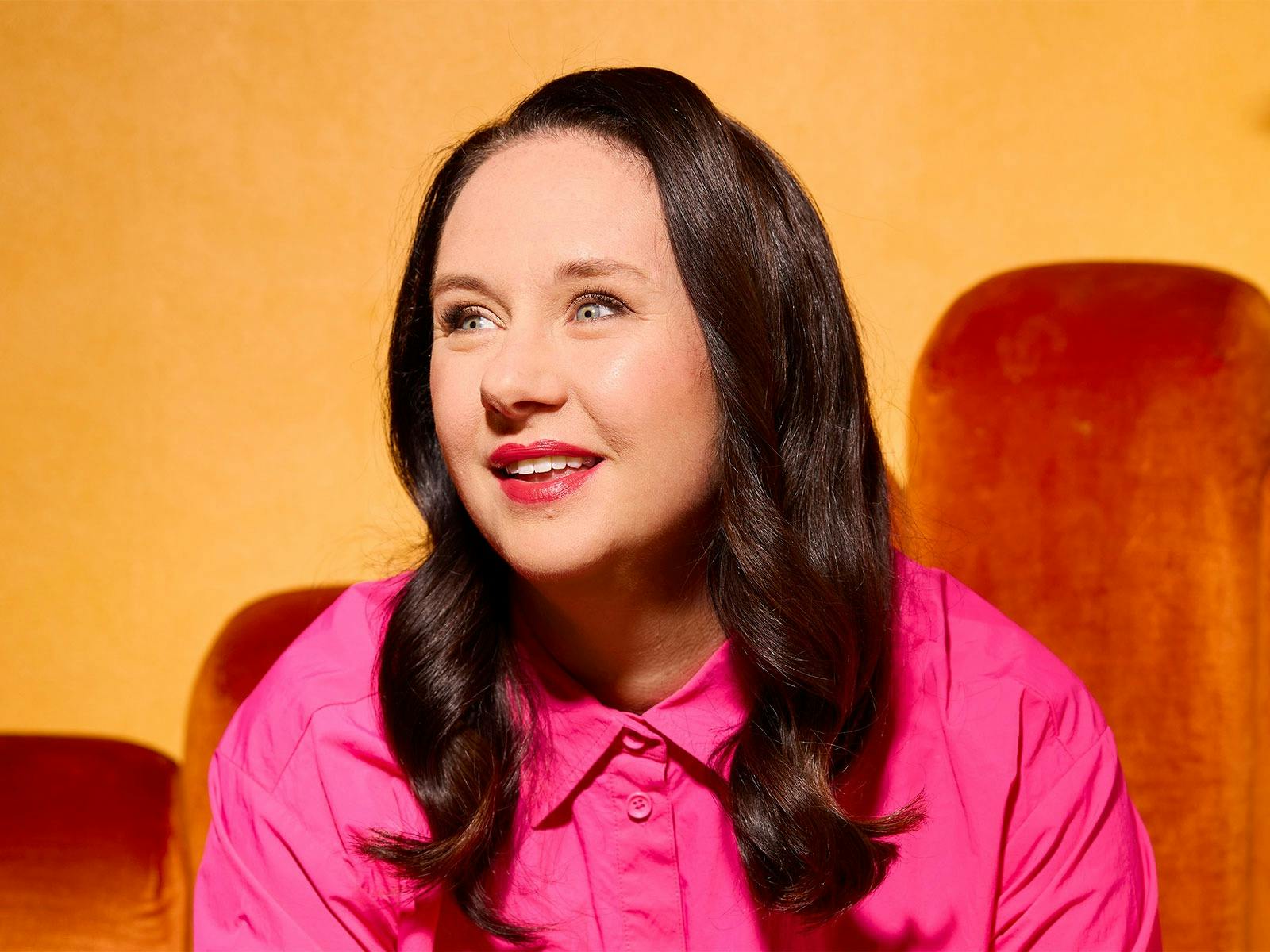 A head shot of a white woman with dark brown hair, she's wearing a pink button up blouse