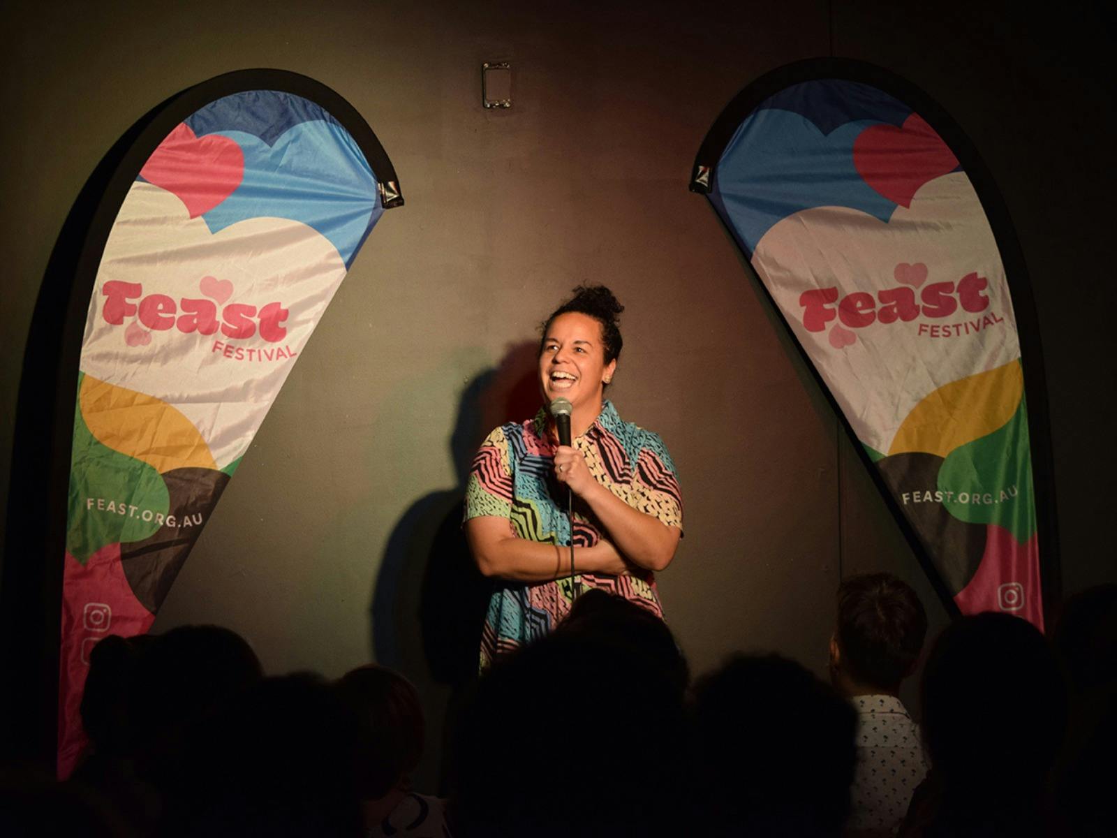 A performer with a colourful button-up shirt laughing into the mic.