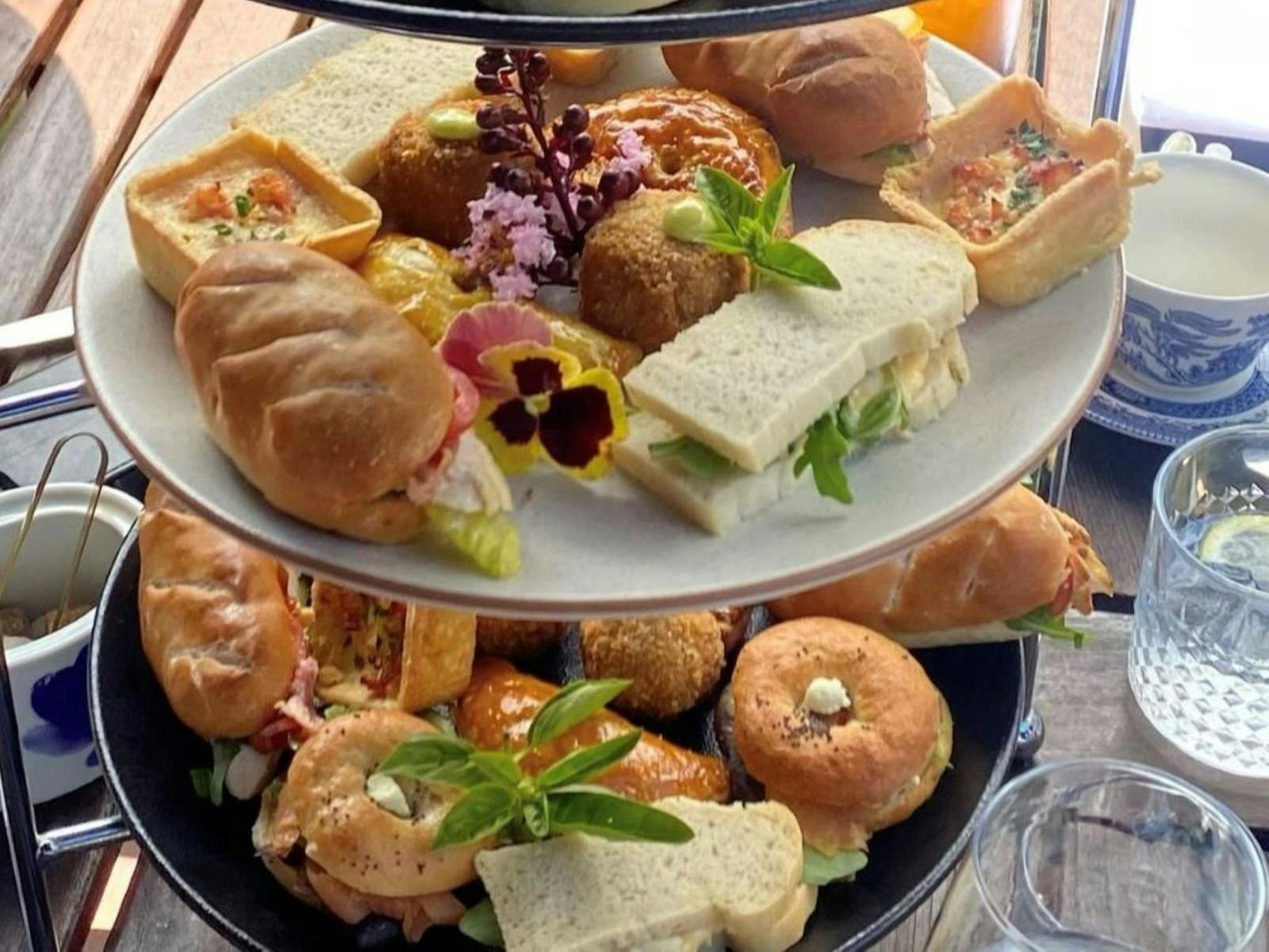 2 tiers of savoury high tea items incluidng bagels, ribbon sandwiches and quiches