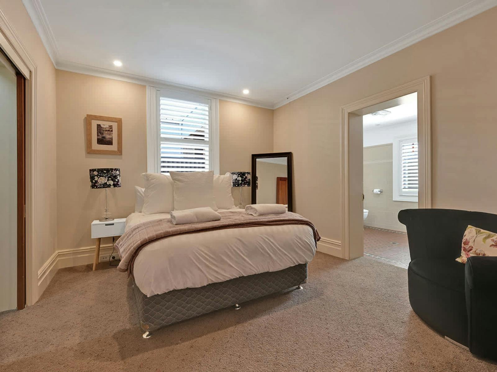 Queen bed with ensuite, lots of windows, mirror, and armchair