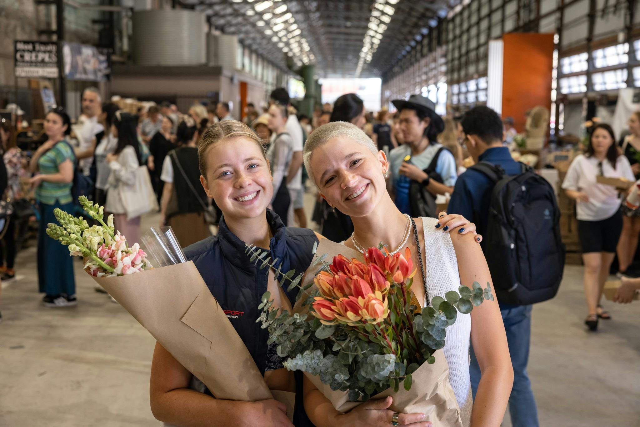 Two girls smiling, holding flowers from the markets