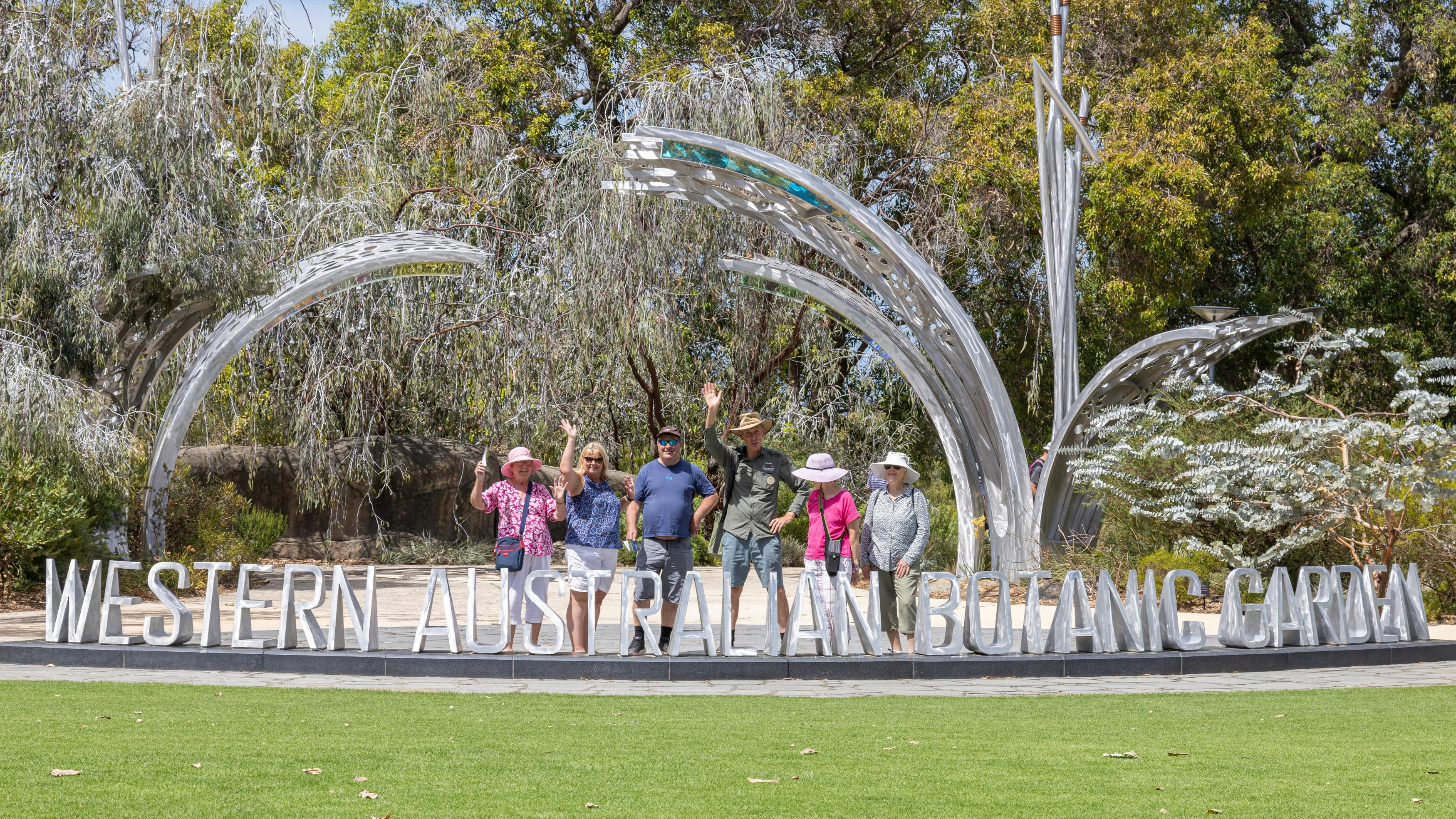 A group of visitors and a Guide smiling and waving at the silver letters marking the garden entry