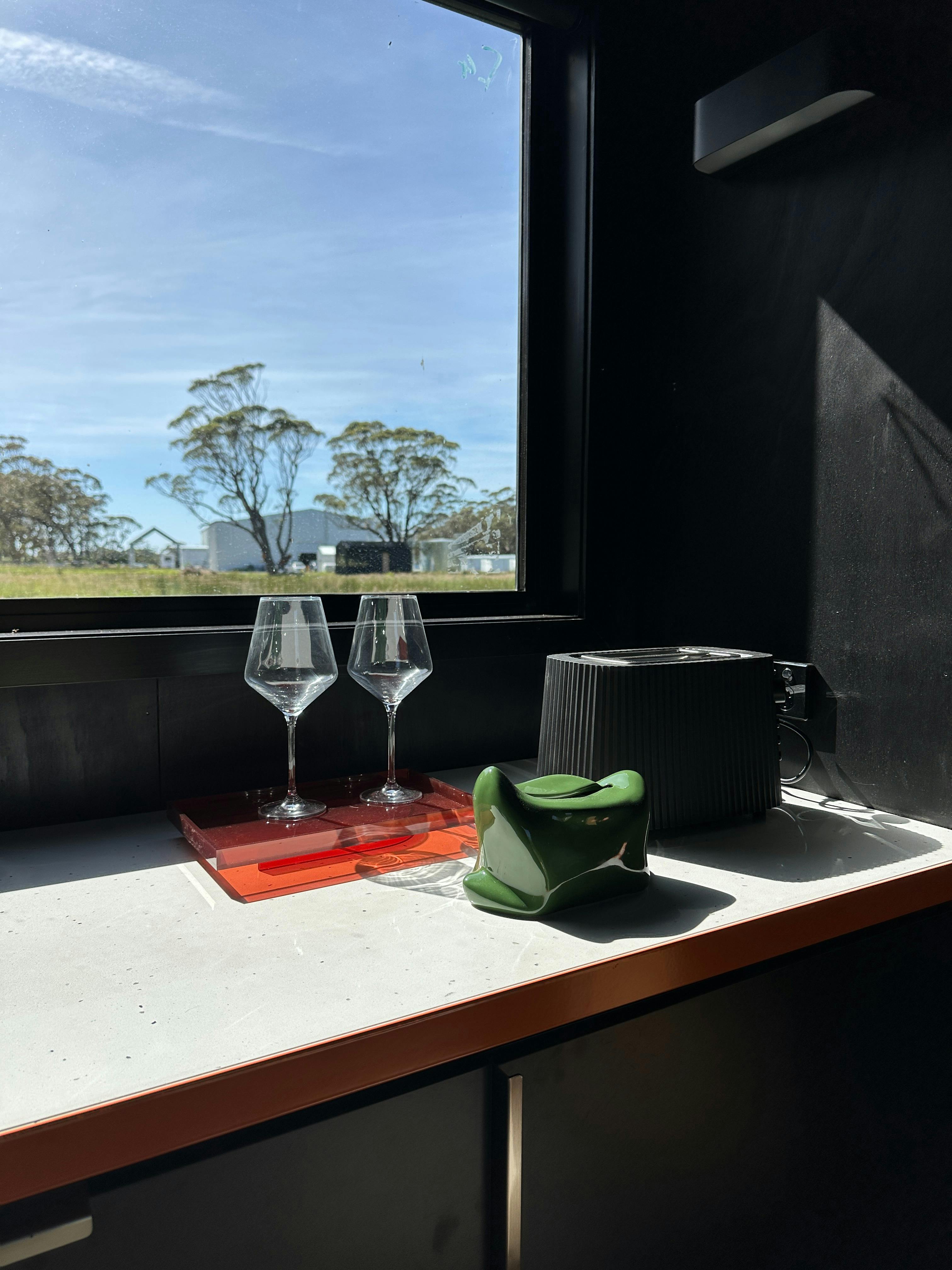 A stone kitchen benchtop with Alessi toaster, wine glasses and tissues box