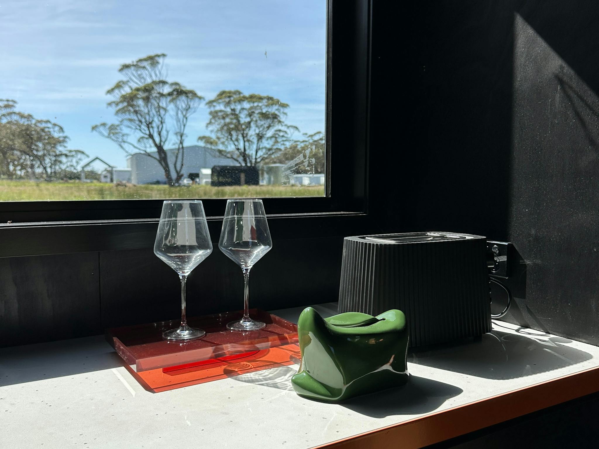 A stone kitchen benchtop with Alessi toaster, wine glasses and tissues box