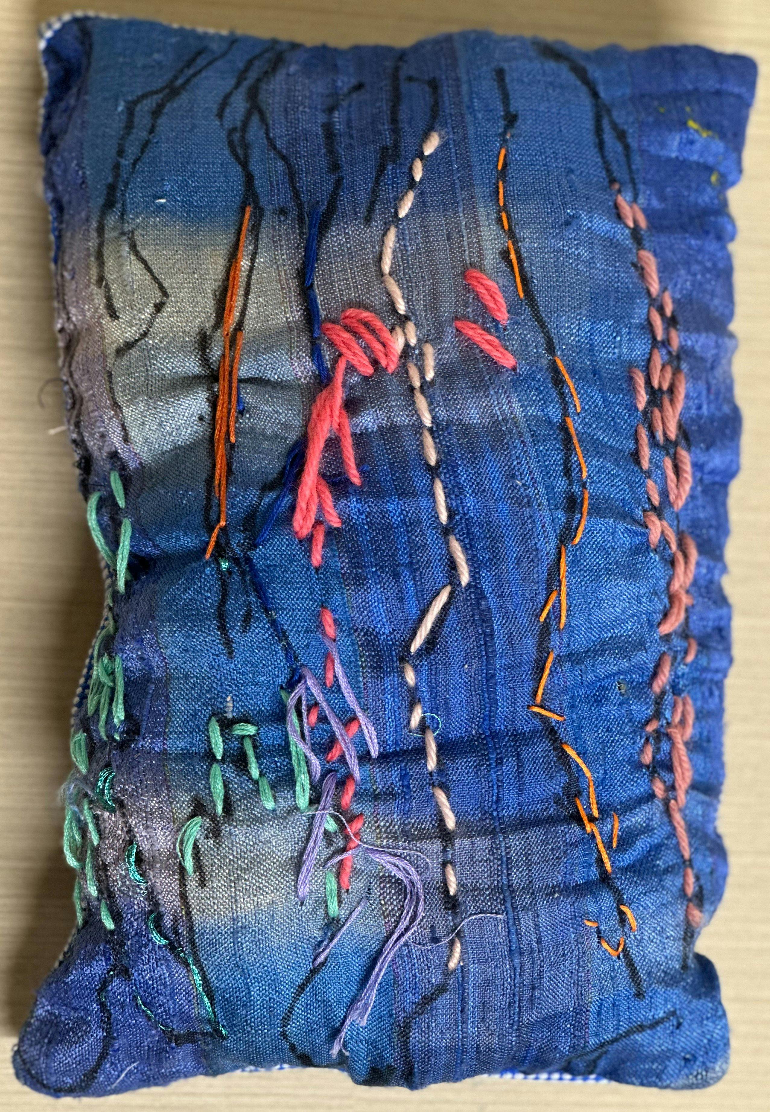 A blue fabric cushion with coloured stitching on the cover.