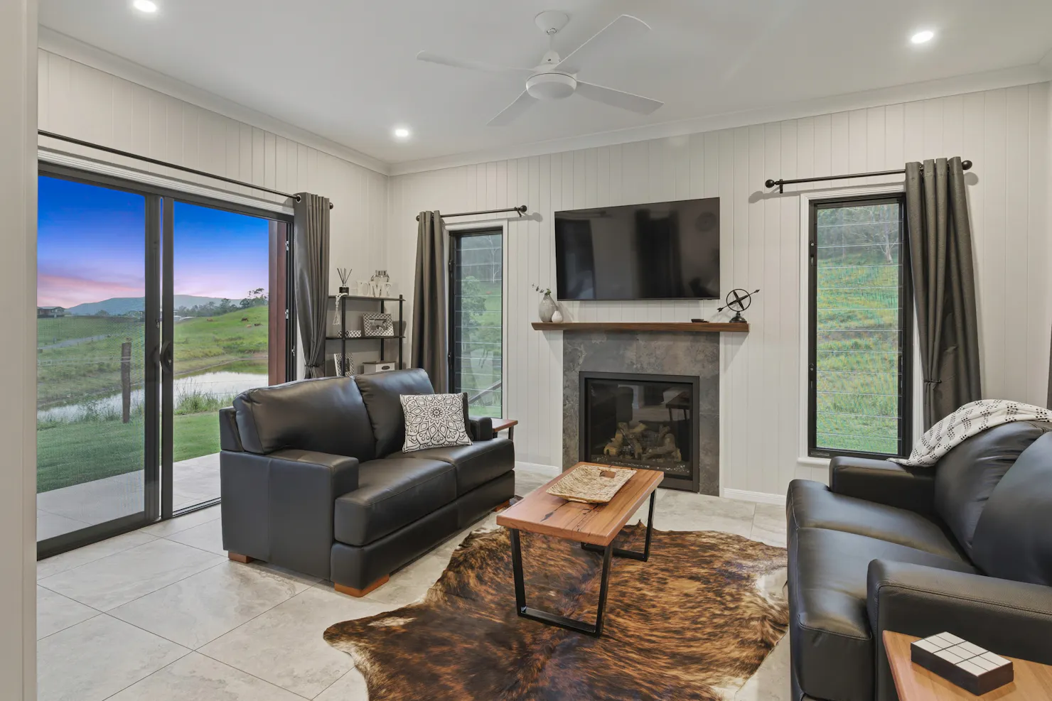 Living room with leather sofas, fireplace, and large windows overlooking farmland