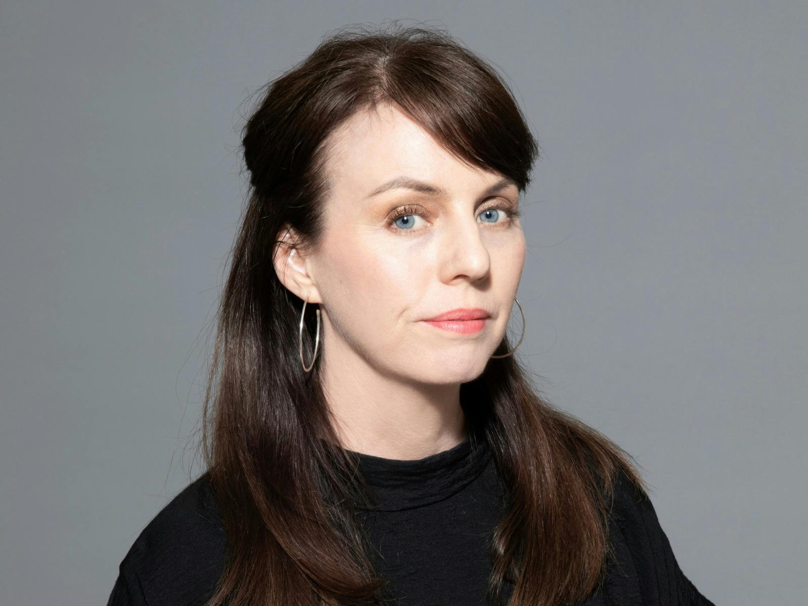 Studio portrait of Petrina Hicks wearing a black top against a grey background.