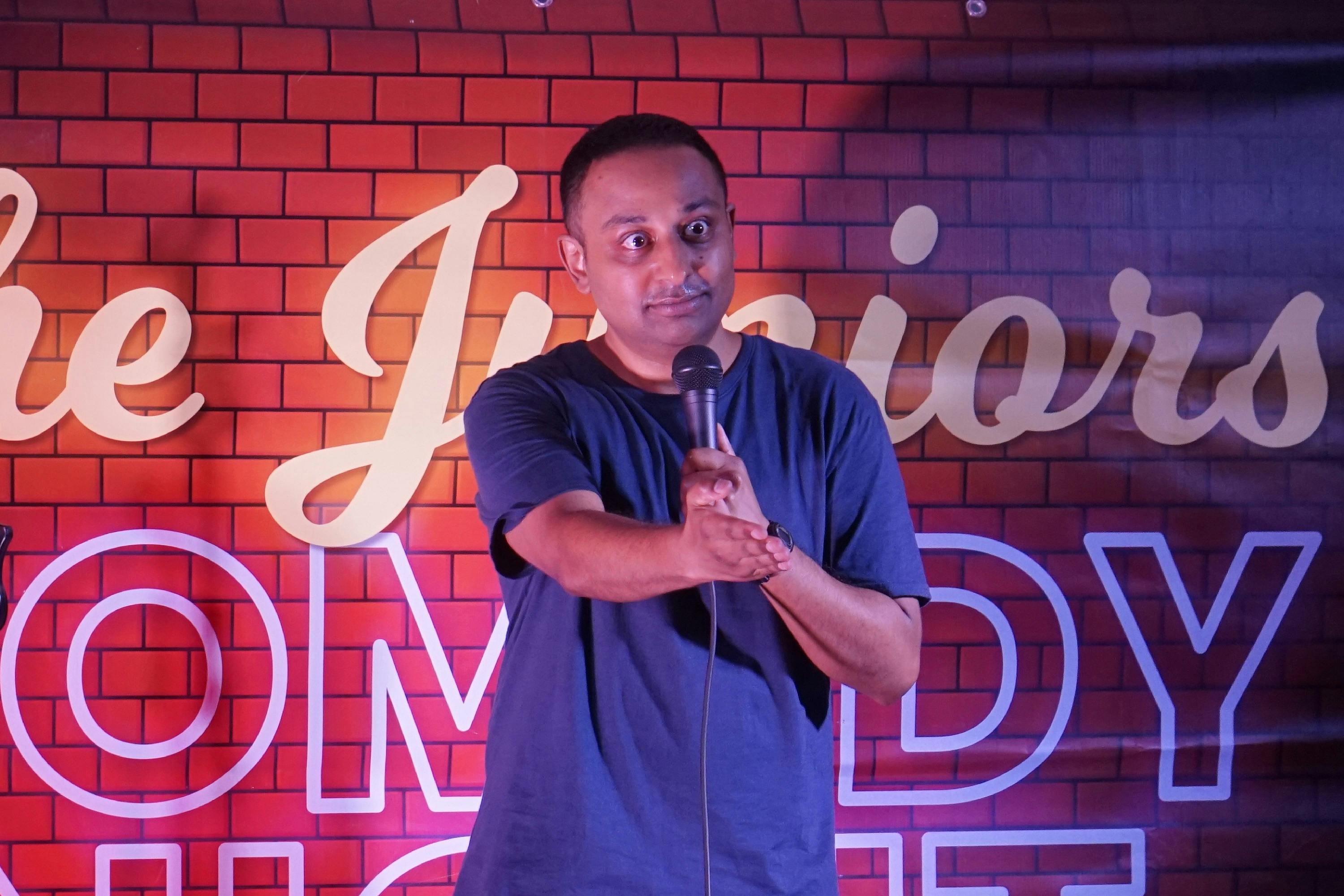 Comedian Umit Bali gestures curiously at the audience while he perfroms at Maroubra Comedy Club