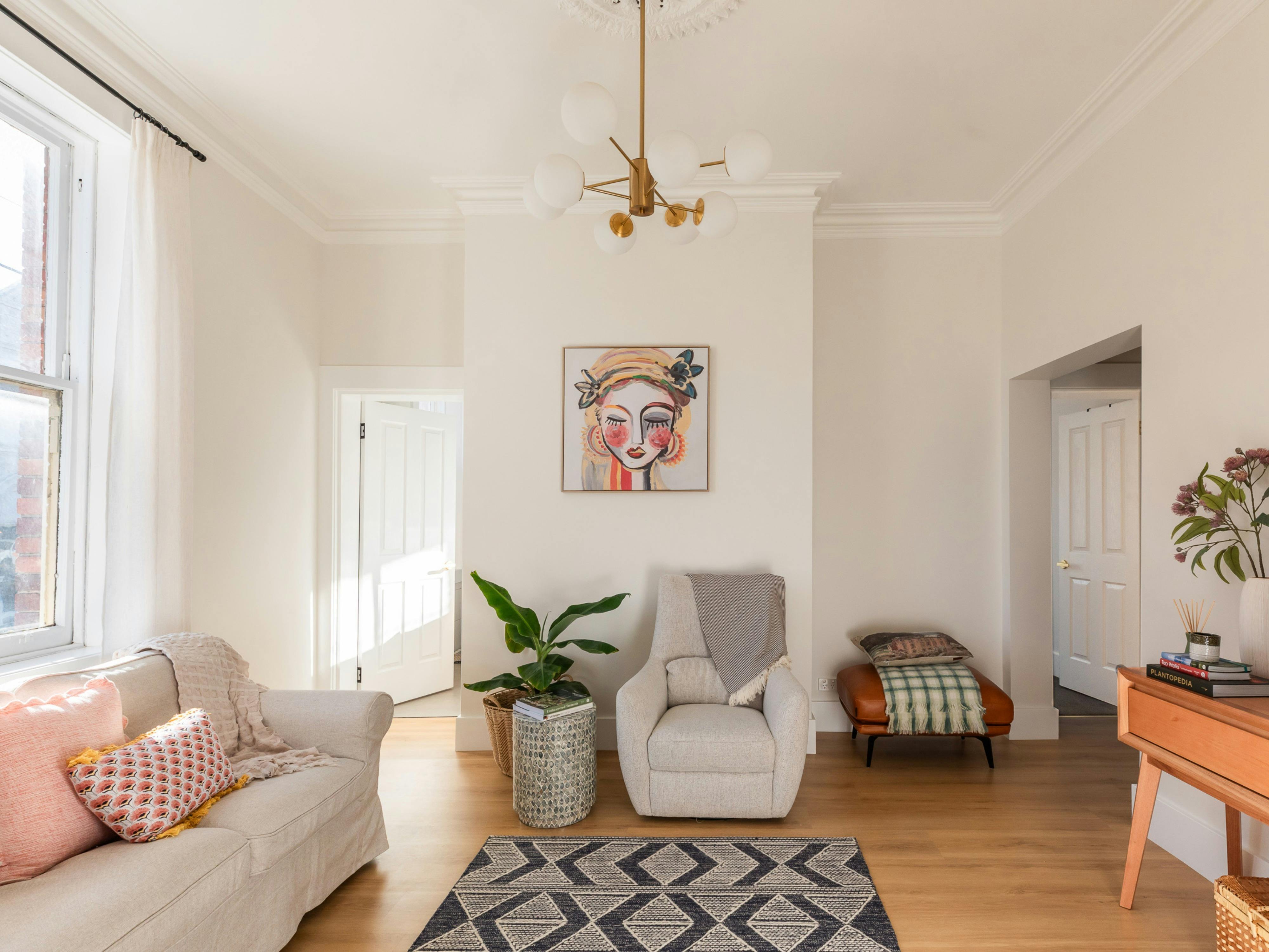 Living room with sofa, occasional chair, plant, chandelier, light curtains
