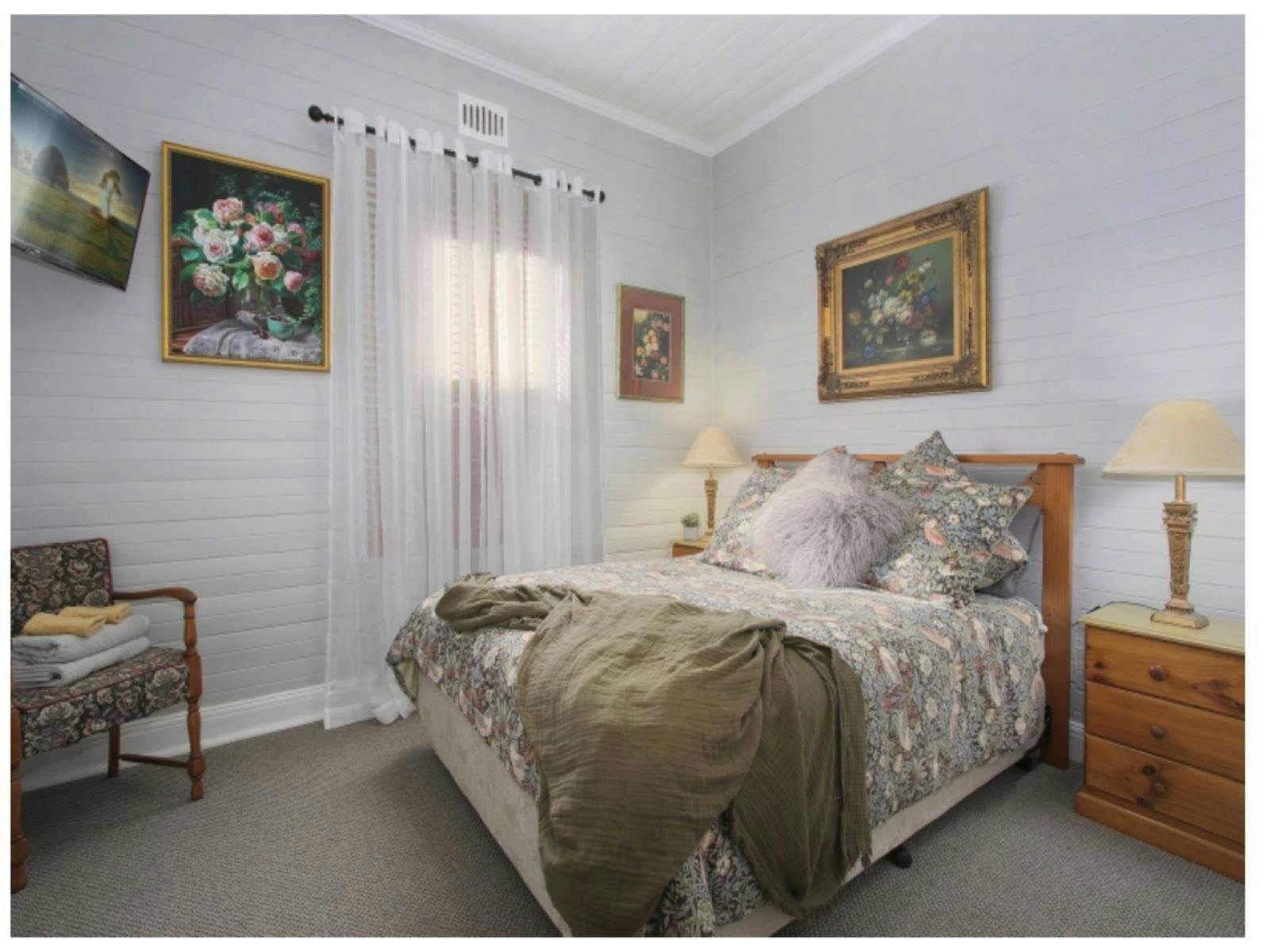 Bedroom, double bed with floral linin, wooden bedside table, television and a seat.
