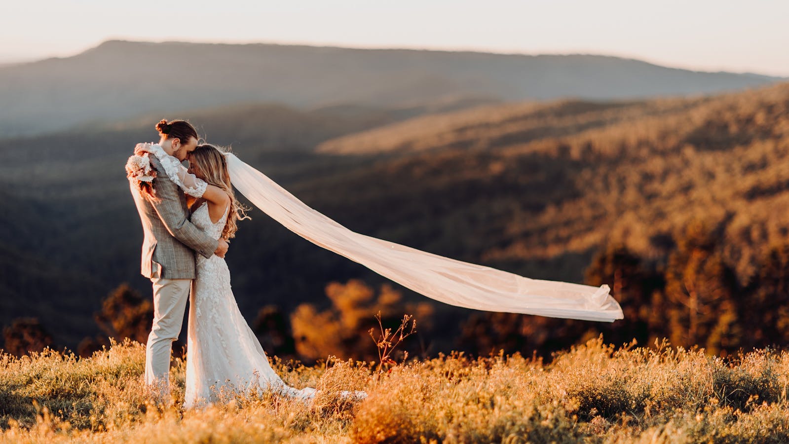 Orange sunset, groom embracing bride with veil flowing.