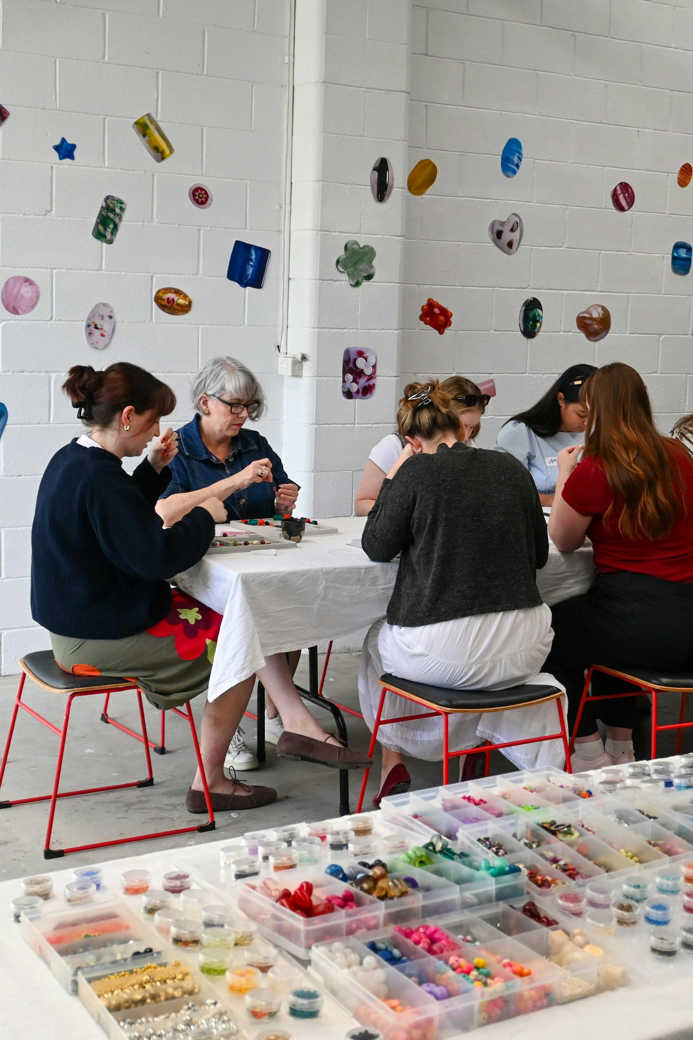 Women sitting around a table making necklaces.