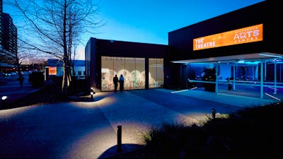 A couple look at the window gallery at the entrance of the Belco Arts Theatre on a clear night.