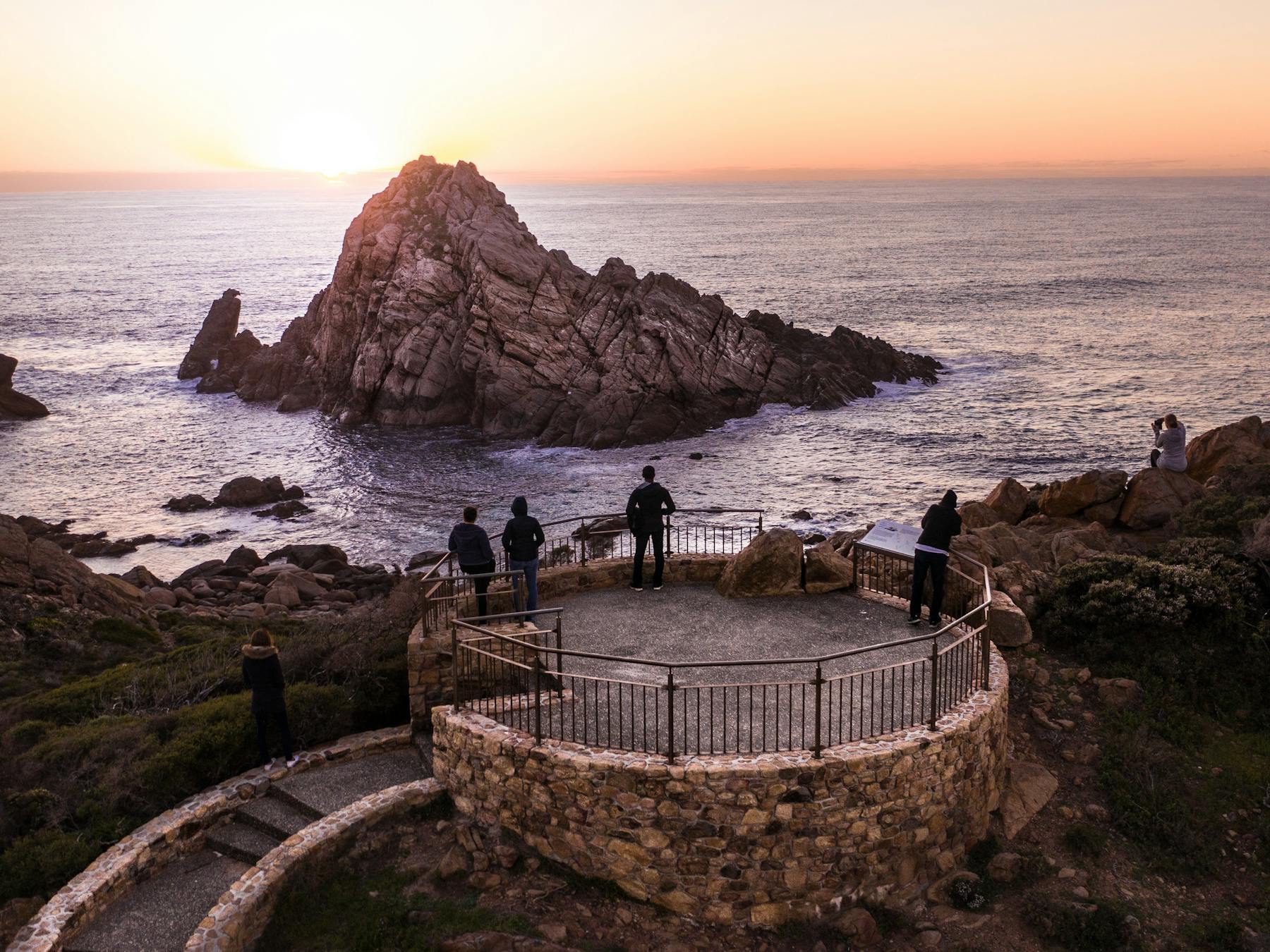 People standing on a lookout overlooking the ocean and a large granite rock/small island.