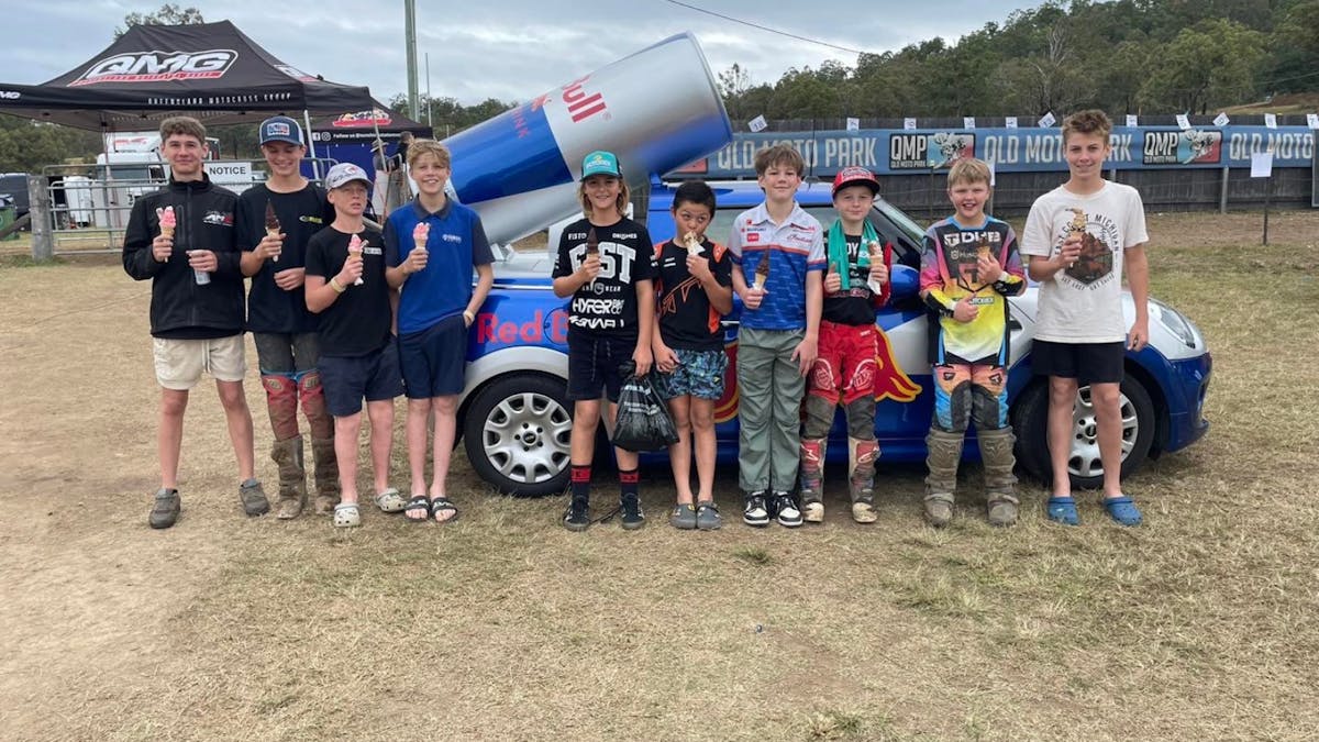 A group of boys in motocross gear and casual clothing smile while holding soft serve ice cream cones