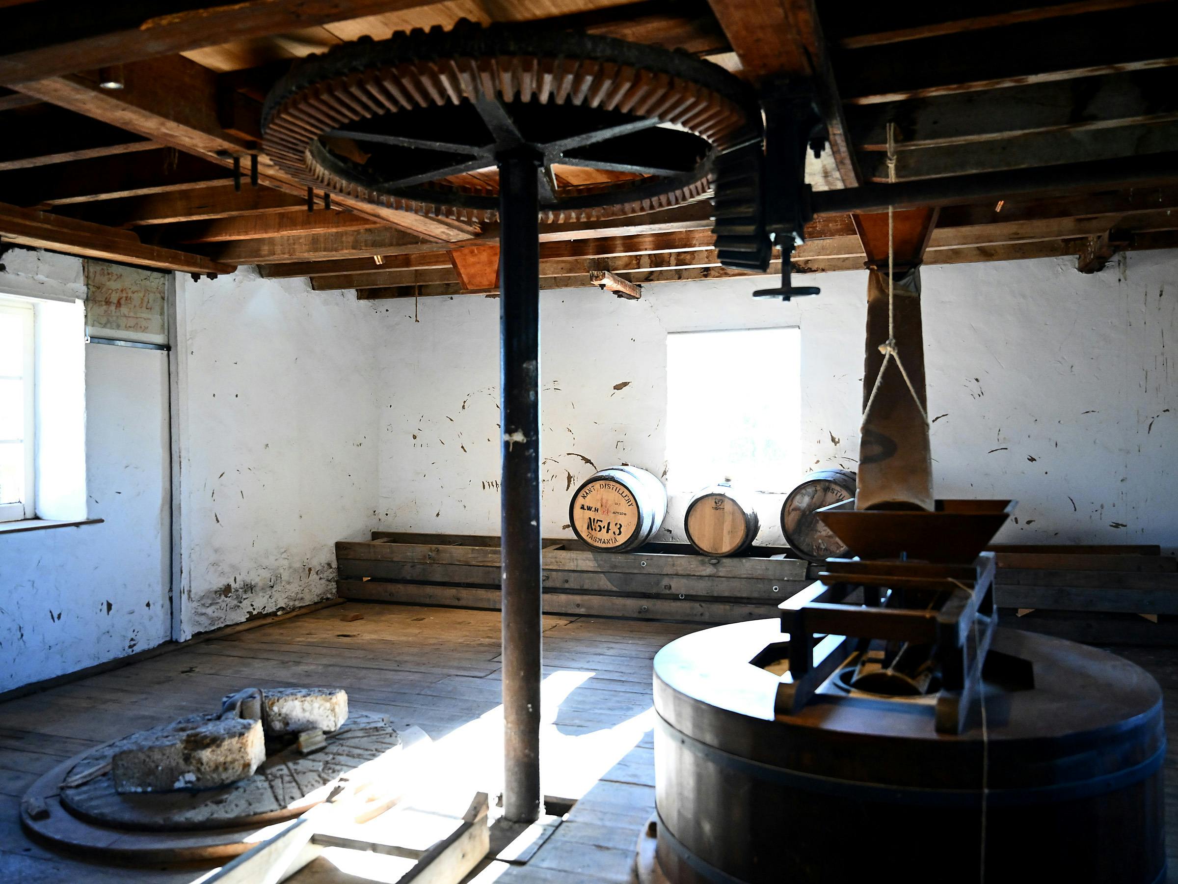 Old mill machinery with whisky barrels in the background.