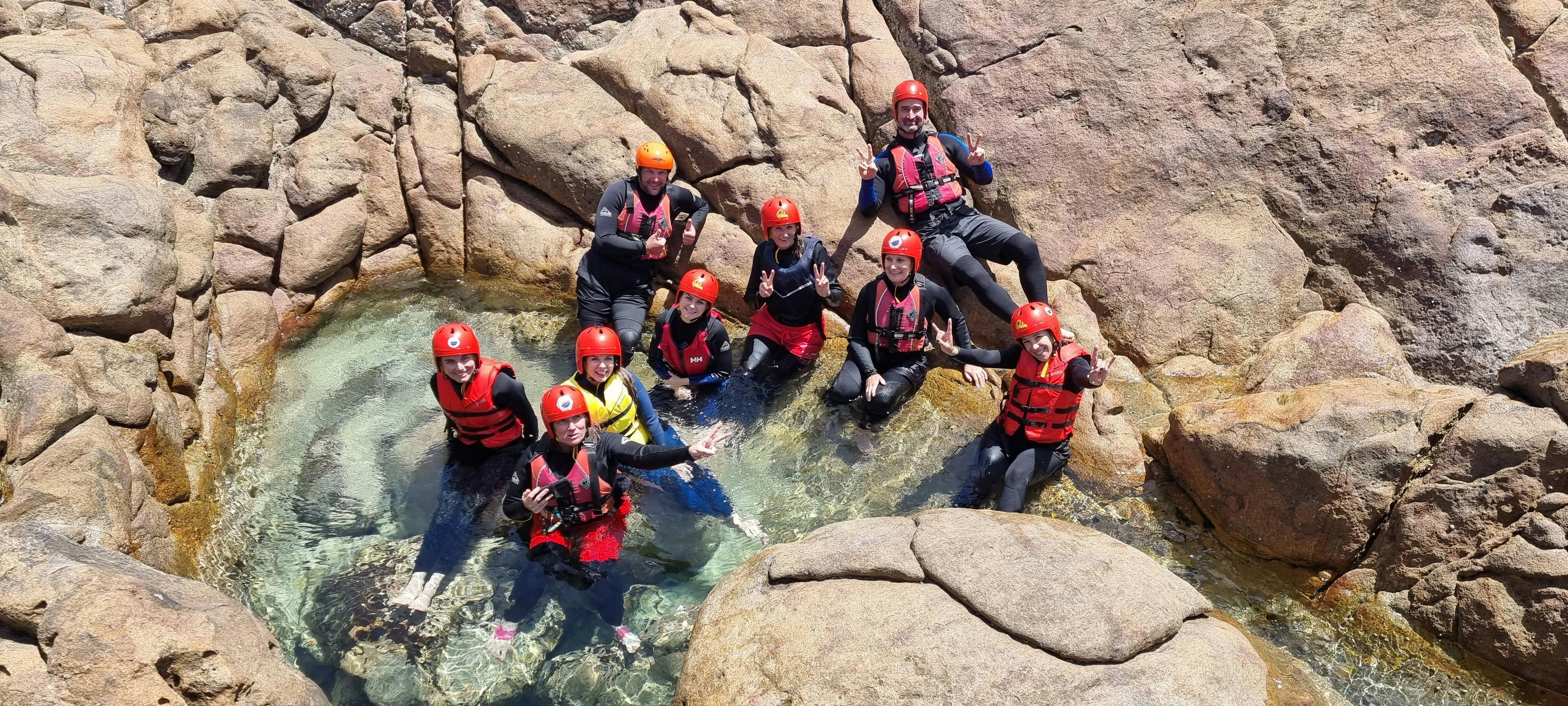 Coasteering group with helmets and lifejackets relaxing in small calm rock pool with clear water