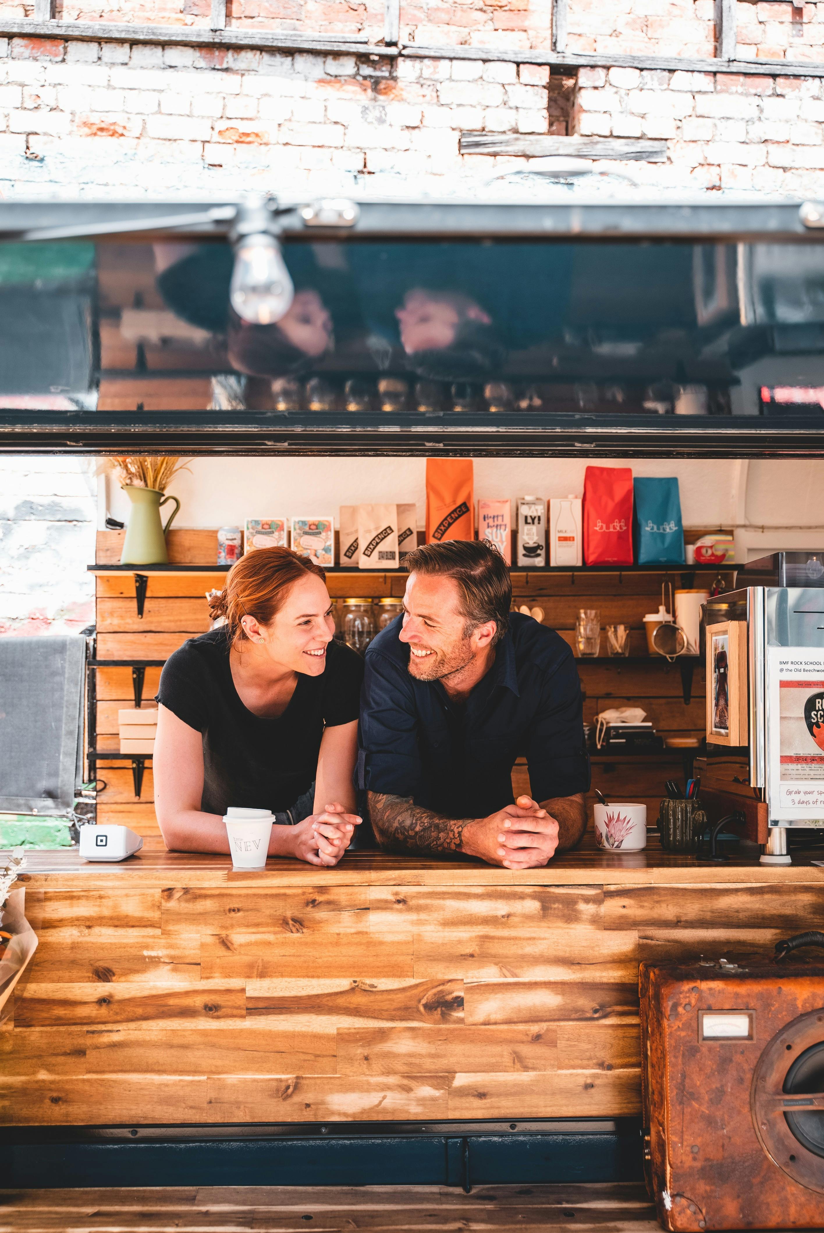 Emma and Michael are smiling, looking at each other inside the coffee van.