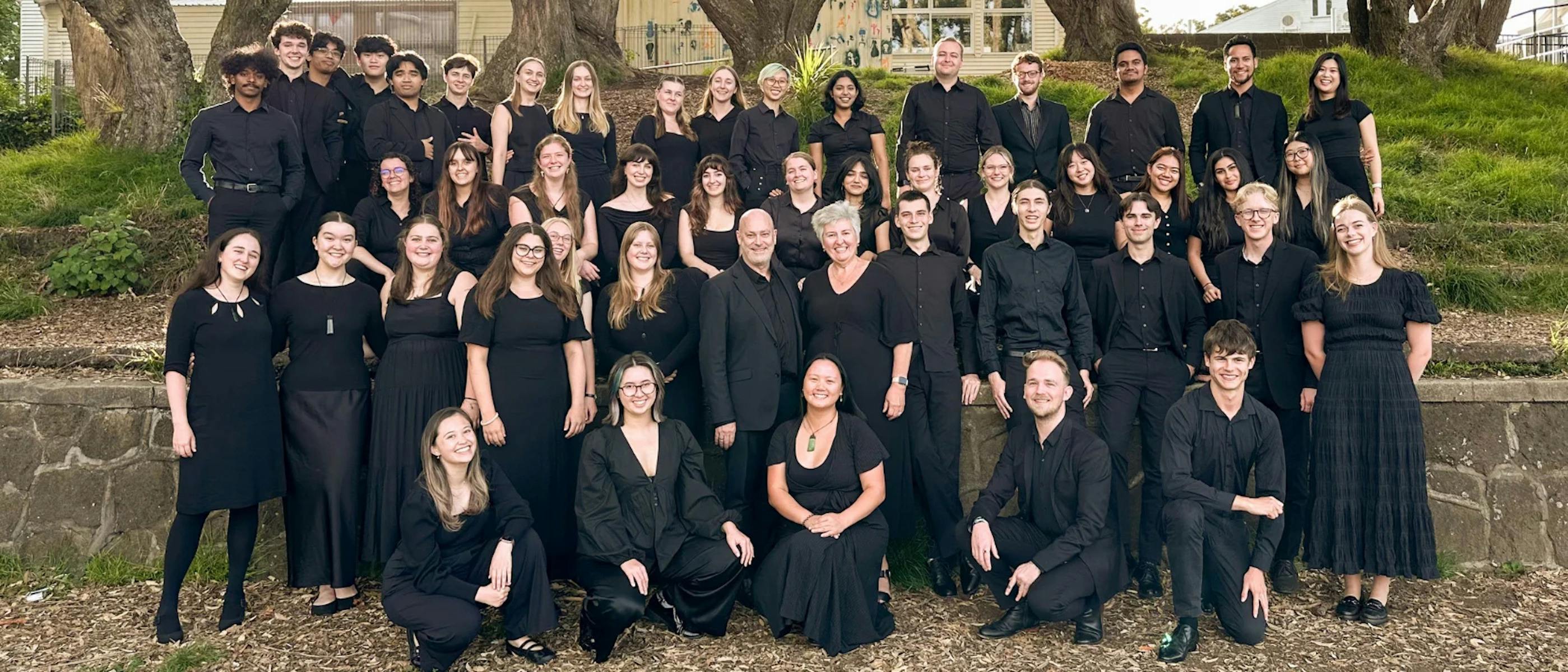A large choir wearing black, smiling and standaing outdoors