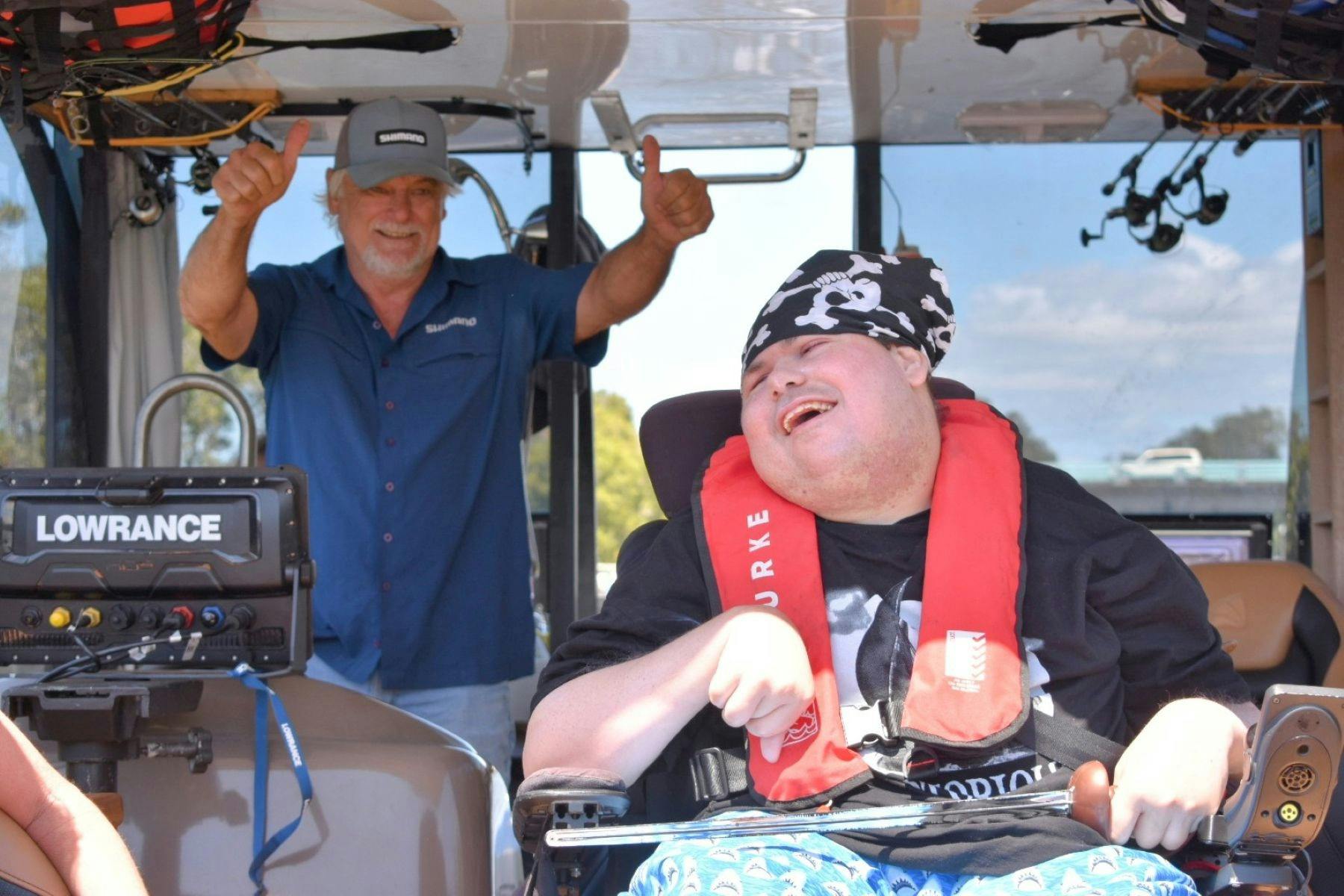 Hookability client smiling on the boat with instructor doing thumbs up in background