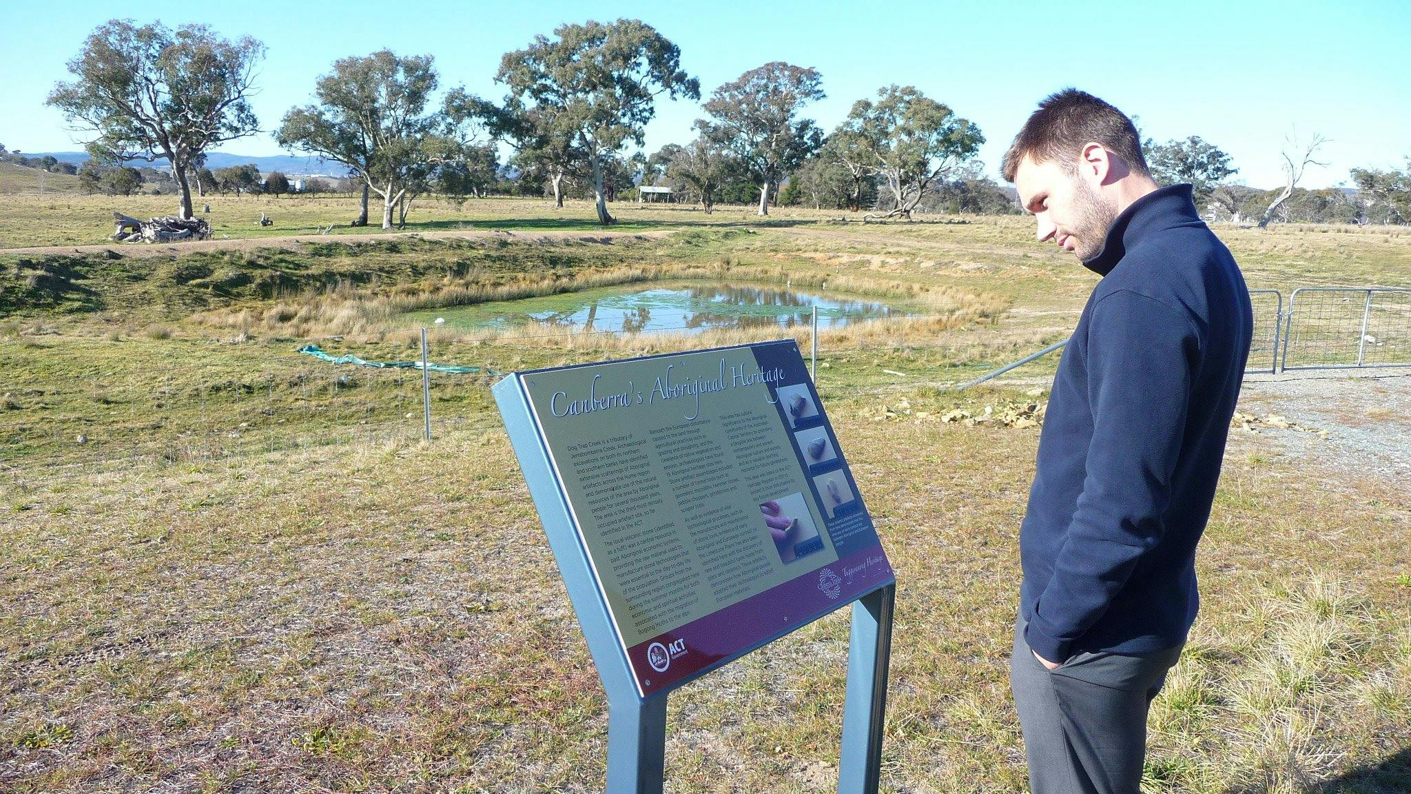 Man reading information panels in grassy area with pond