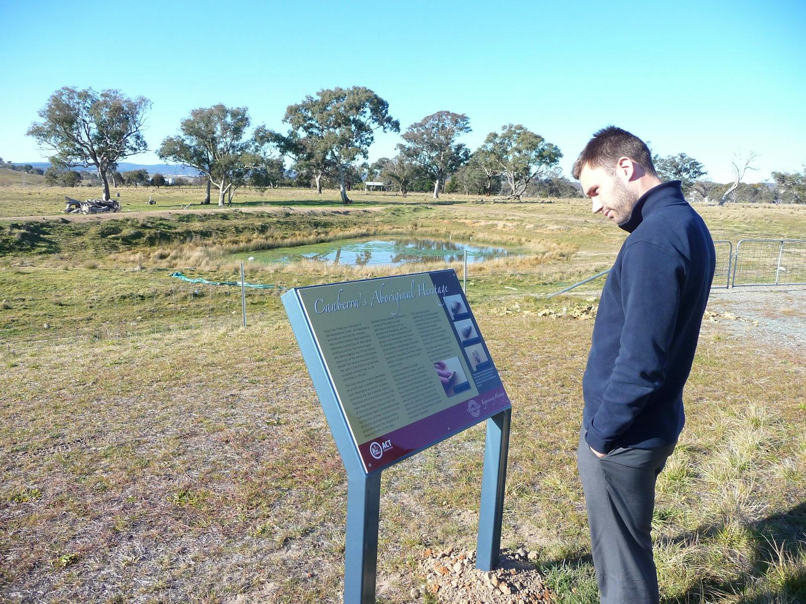 Man reading information panels in grassy area with pond