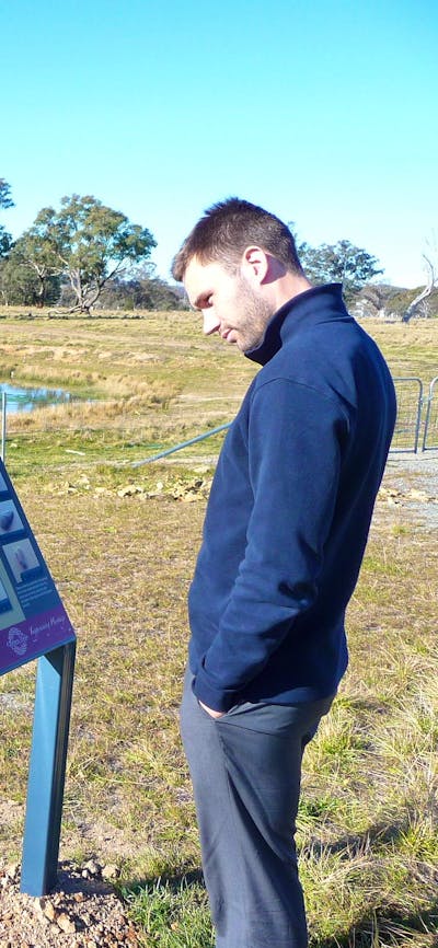 Man reading information panels in grassy area with pond