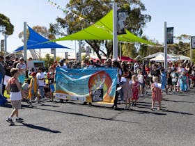 Children and adults parade down a street holding a colourful World Food and Music Festival banner.