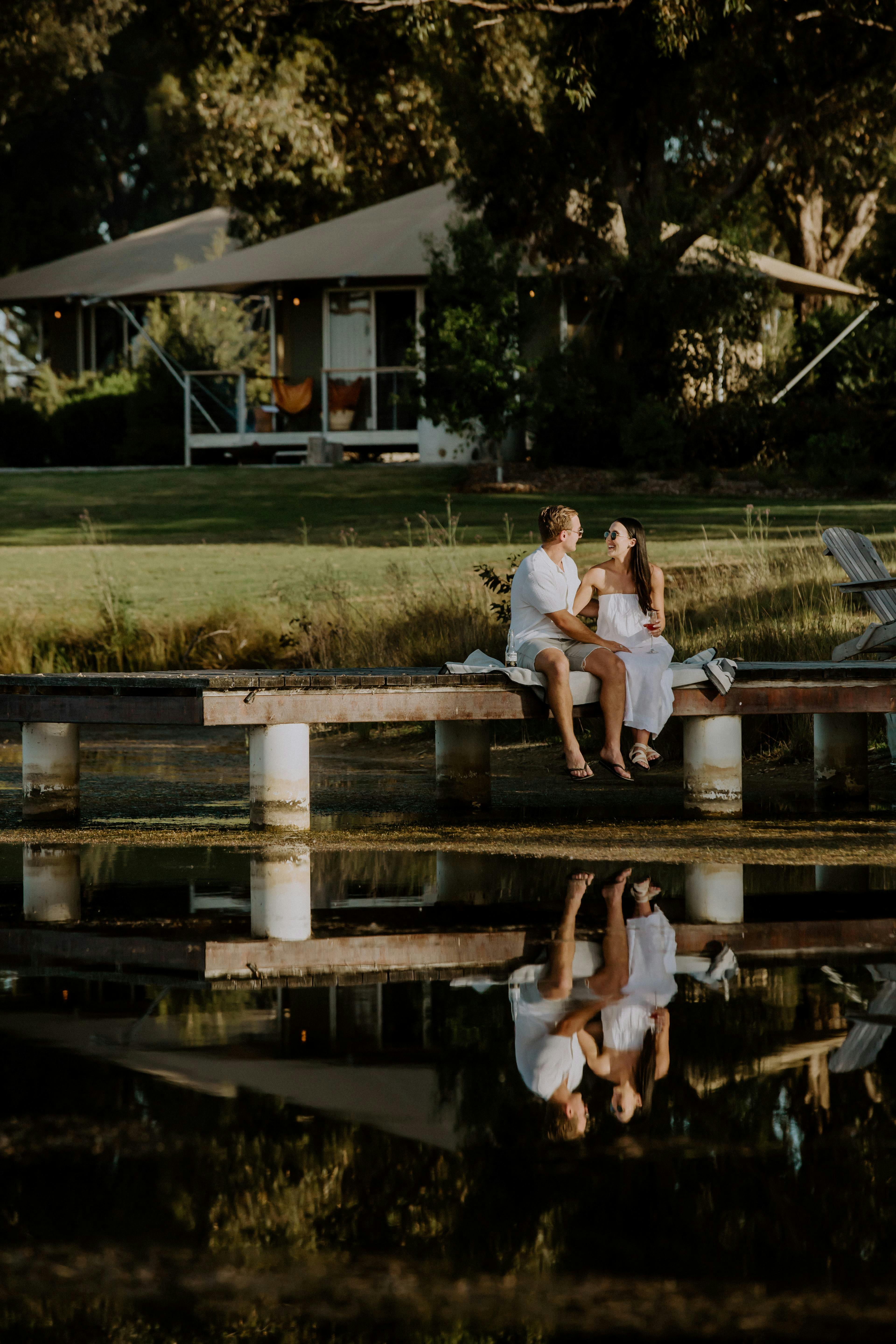 Sunset, couple dressed in white sitting on the jetty feet dangling,and eco tents behind them