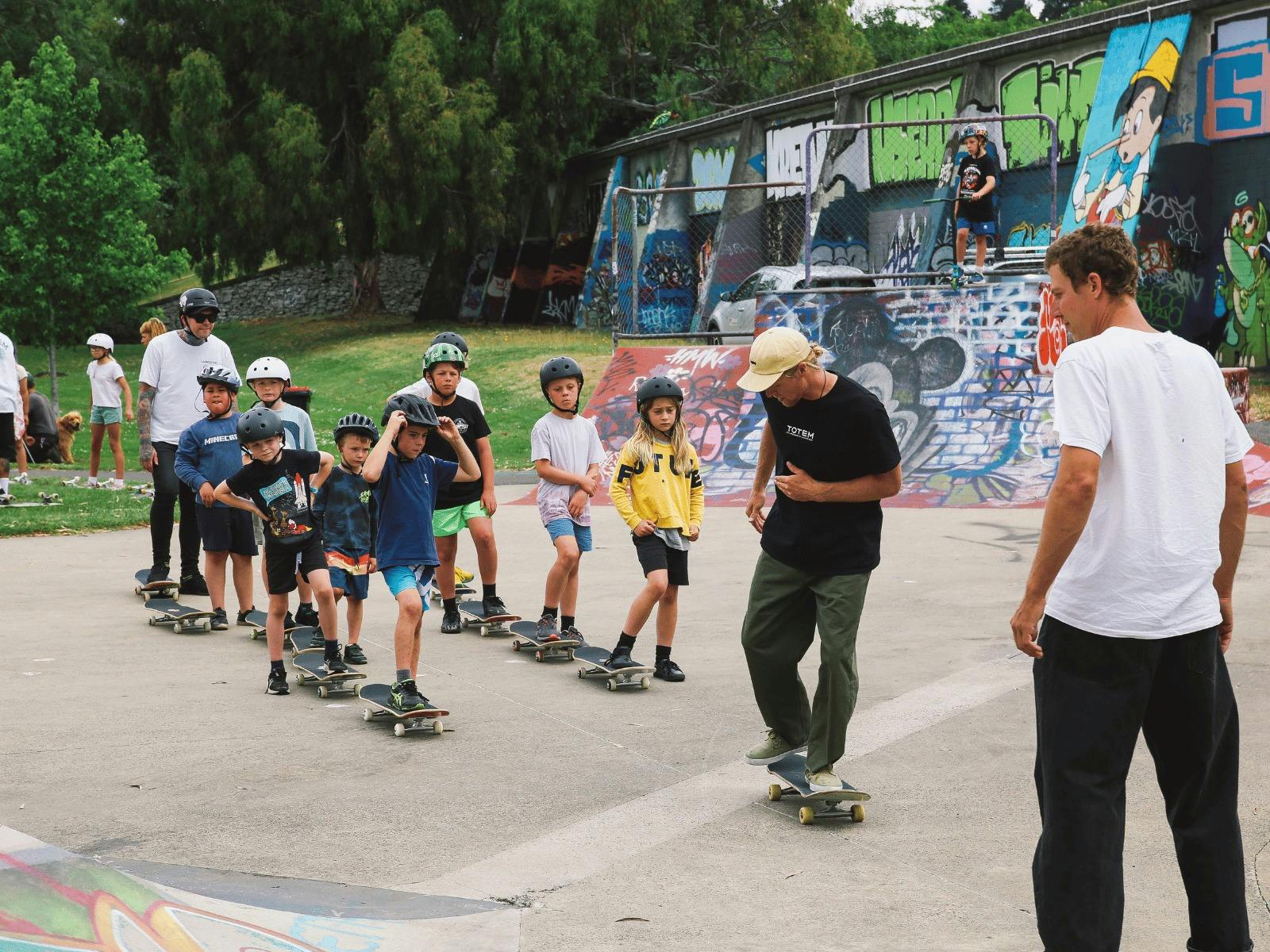 children are in 2 lines with a foot on their skateboard waiting their turn for adult instructor
