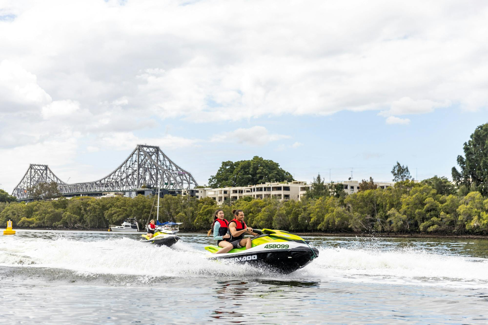 Group of people riding jet skis on Brisbane River with Story Bridge in background.