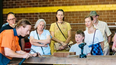 Visitors of all ages enjoying a demonstration by skilled craftsman and staff member