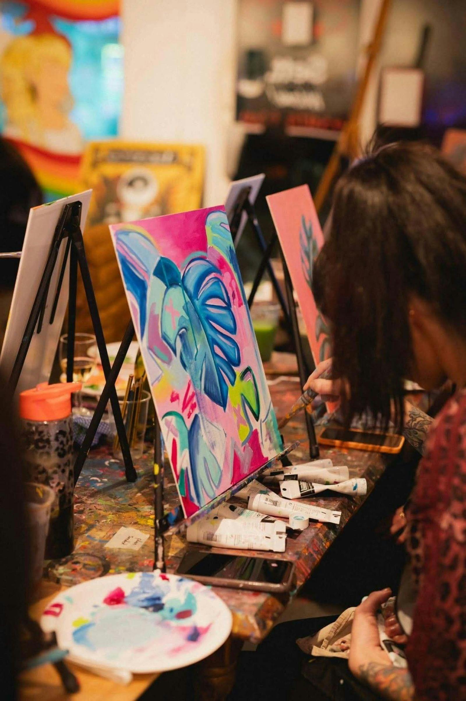 woman with ponytail painting bright coloured picture on canvas