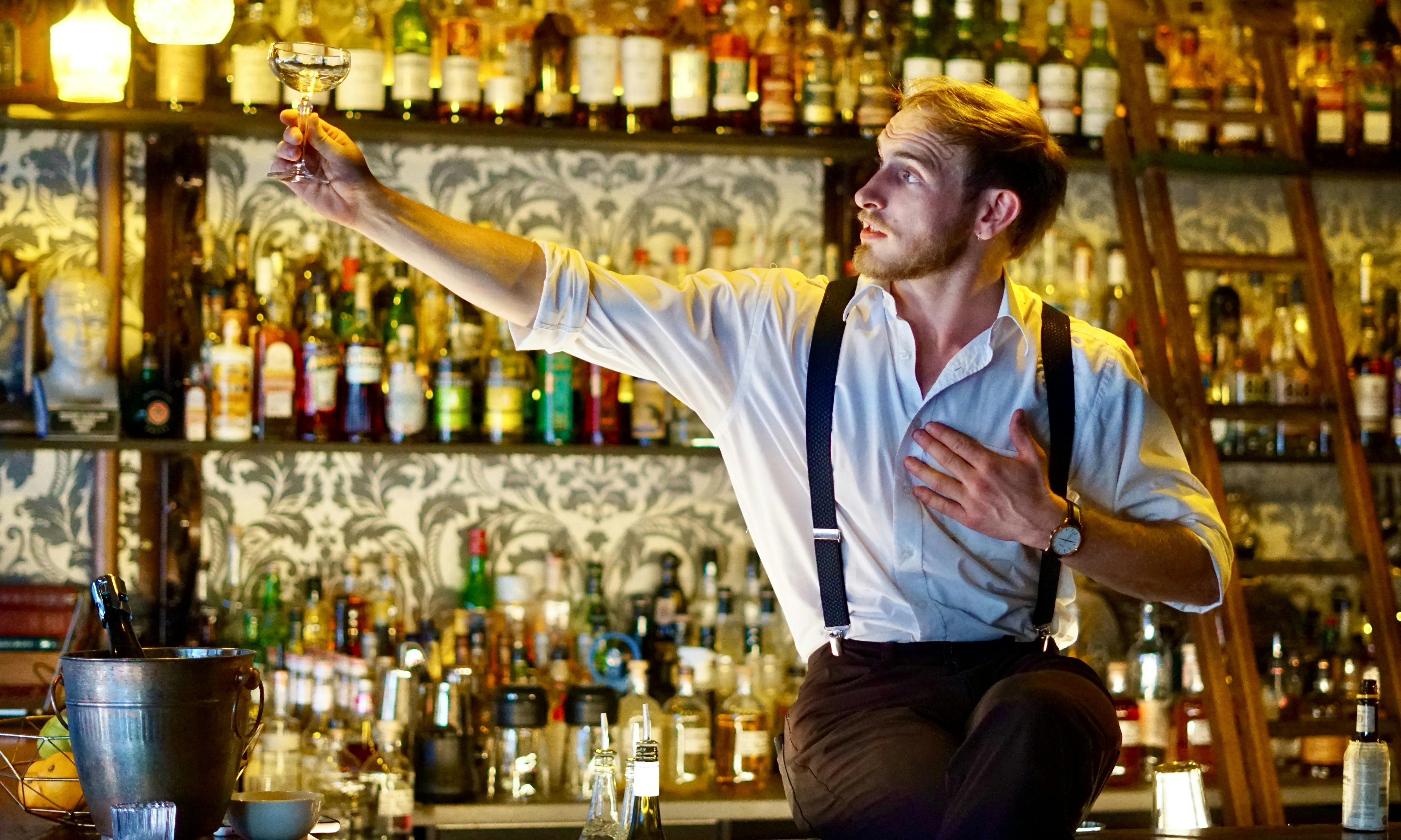 A bartender raises a glass to the light with his hand on his heart
