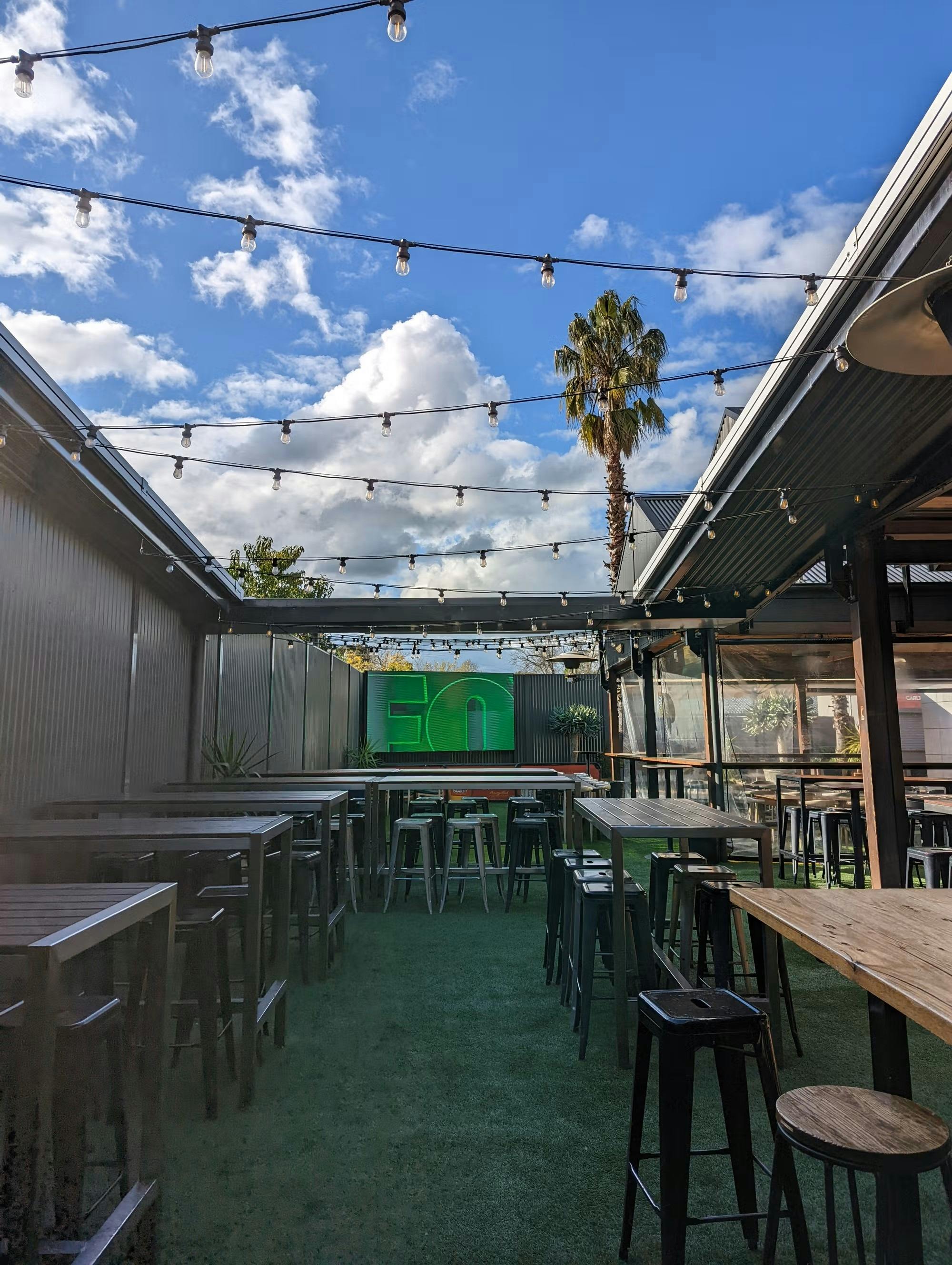 Outdoor seating area with large screen TV,  overhead lights.