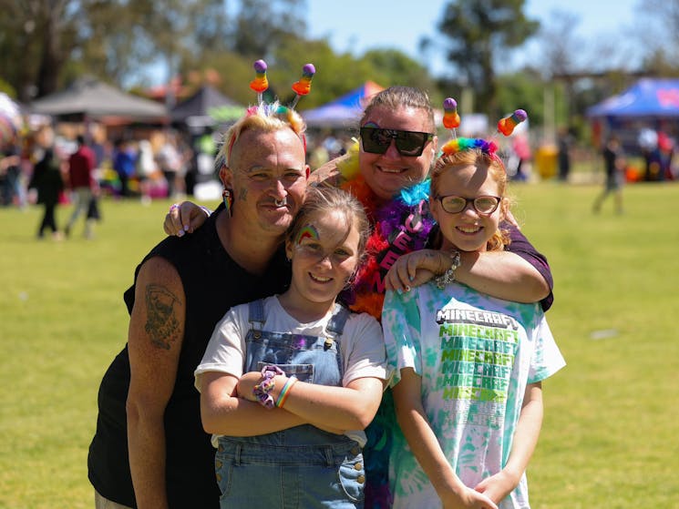 The image shows a family hugging each other all dressed in bright colours in the middle of the park