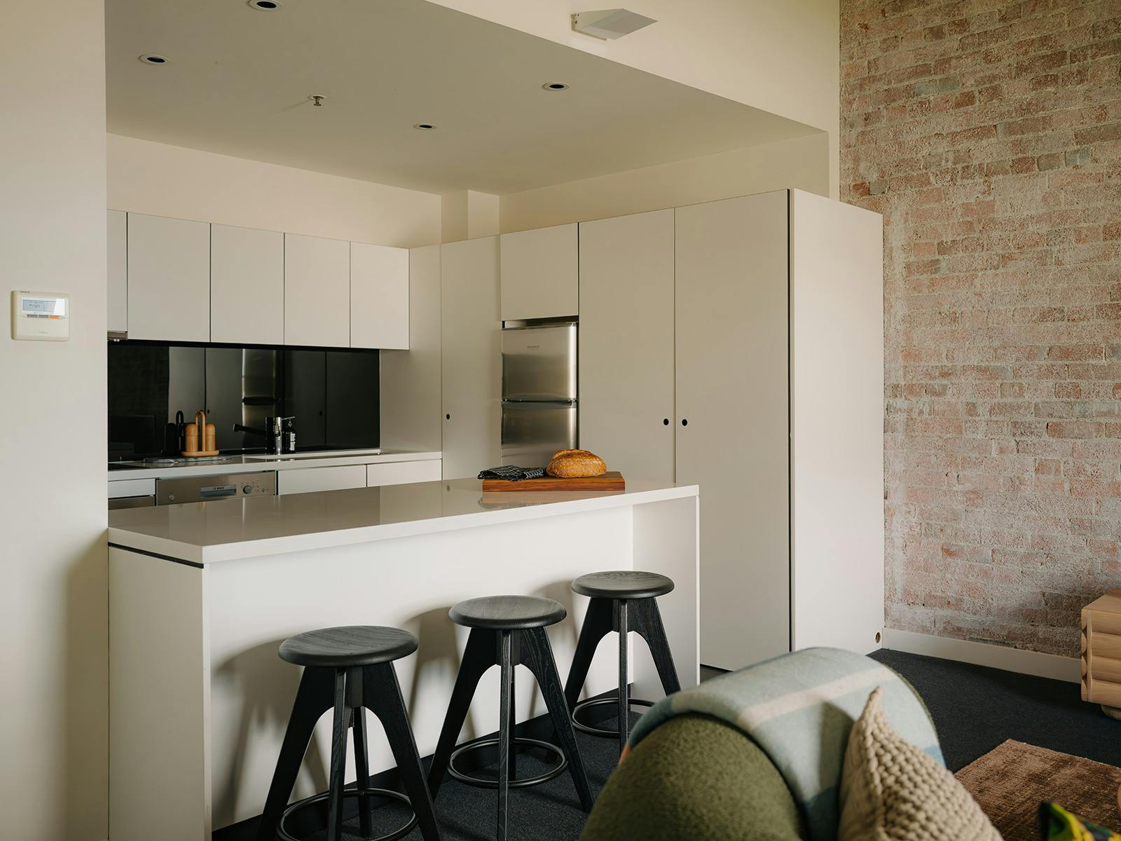 Modern white kitchen with island, bar stools, and brick feature wall.