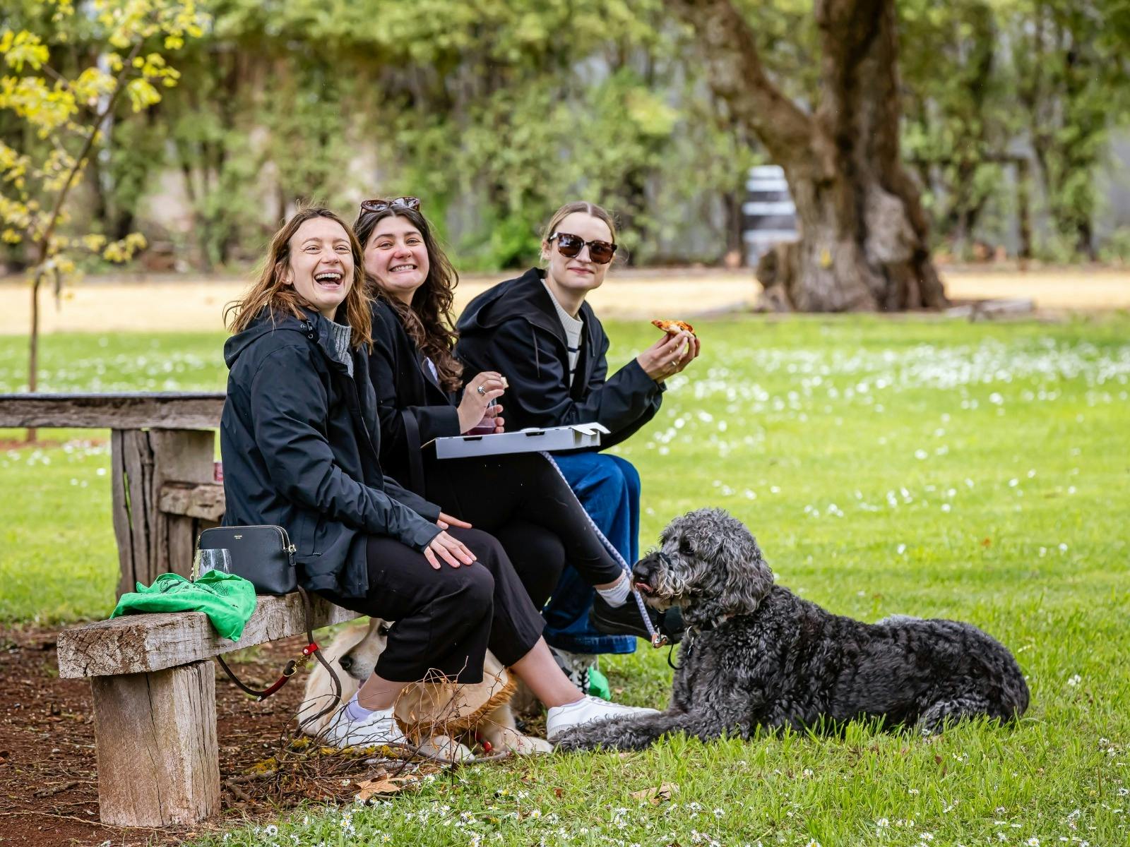 Three women eating pizza with their dog in the Coonawarra Park at the Woof & Wine Walk 2025