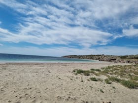 Wide sandy shoreline at Farm Beach under sweeping clouds and clear blue water, calm and open